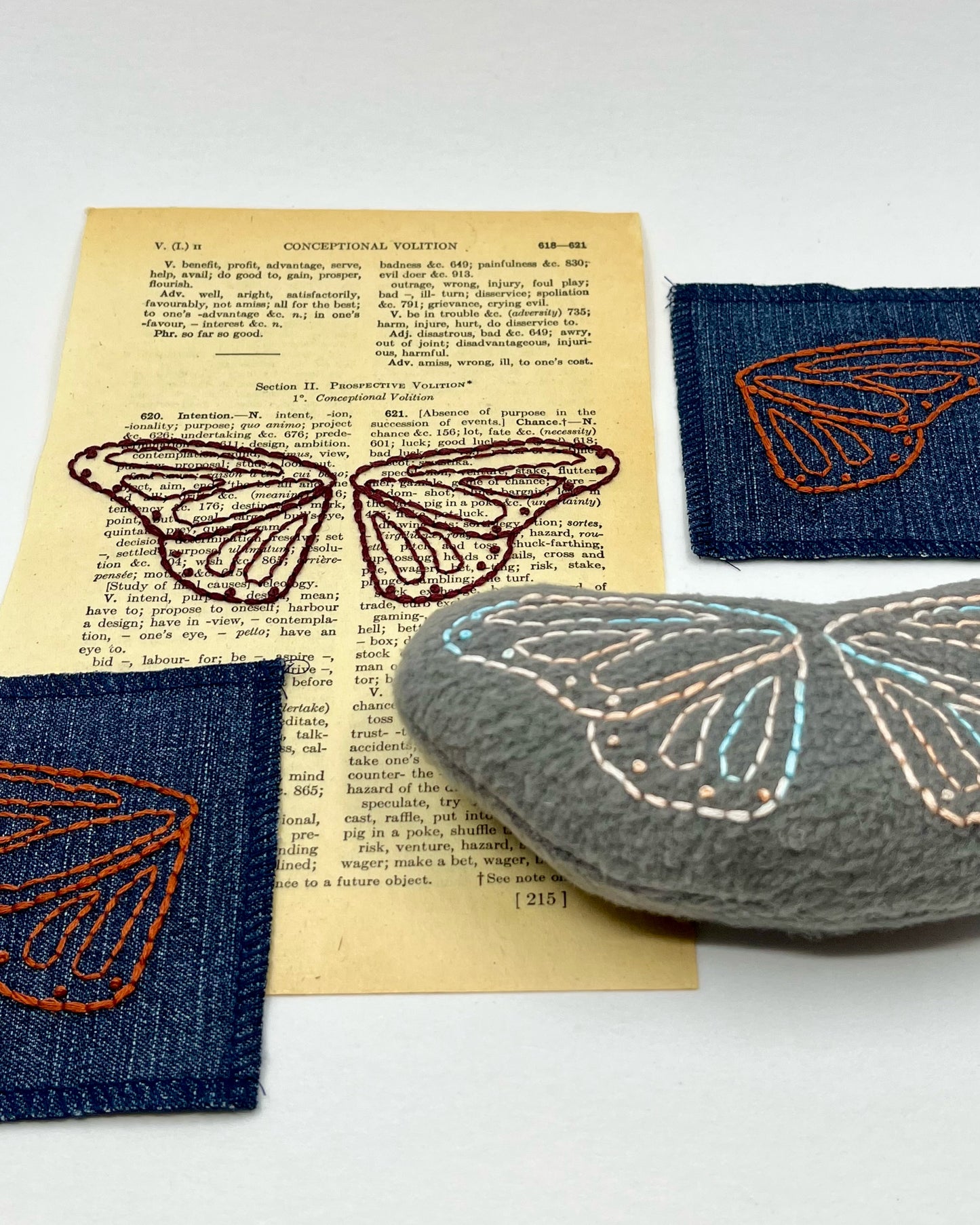 a group of things including a vintage thesaurus page, two denim patches and a grey stuffie hand embroidered with butterfly wings
