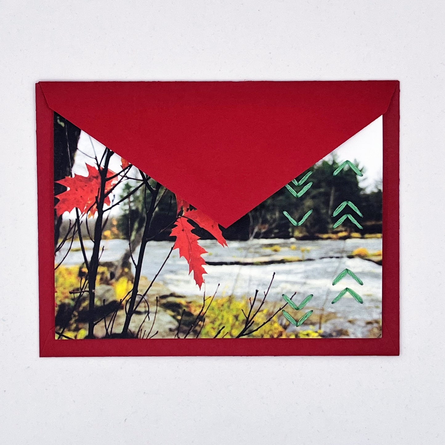 Greeting card flat on an envelope, tucked under the flap. Photo of red leaves. Rows of green chevron stitches along right side card
