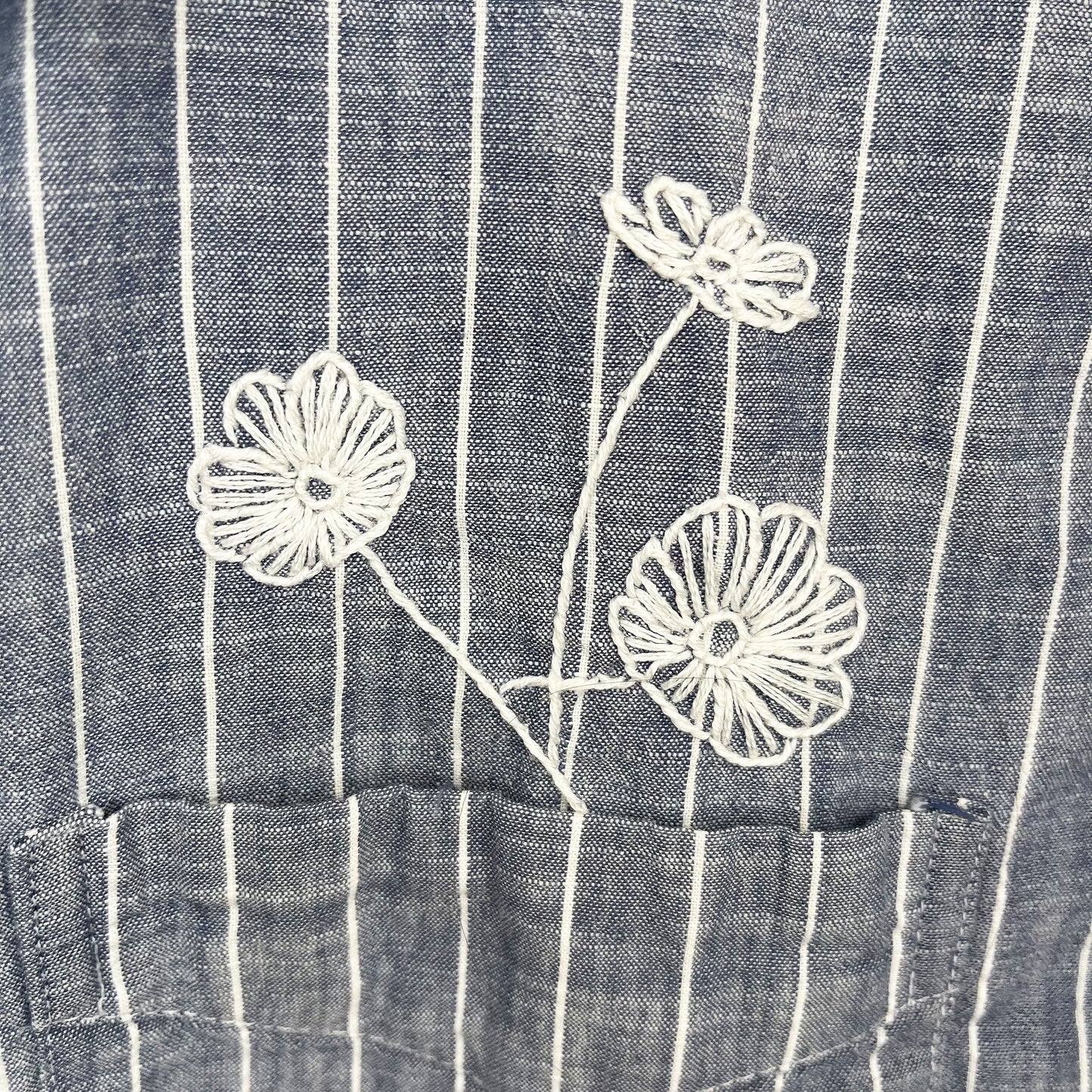 close up view of a striped chambray shirt with white hand embroidered poppies coming out of the chest pocket
