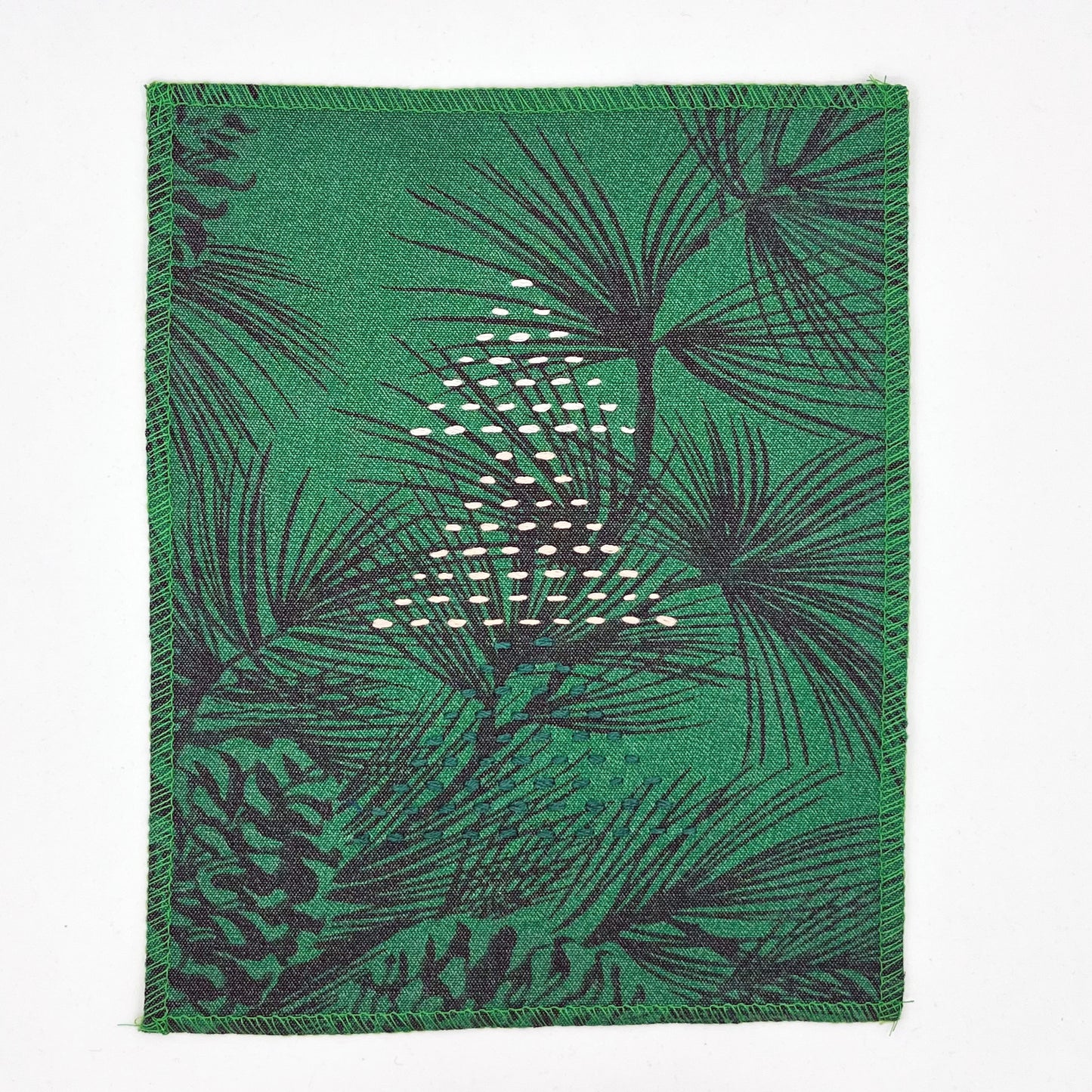 a fabric wall hanging made from bright green fabric with pine branches printed on it, and stitched over with Christmas trees made from three triangles, each triangle made from running stitches in green peach and ivory, on a white background