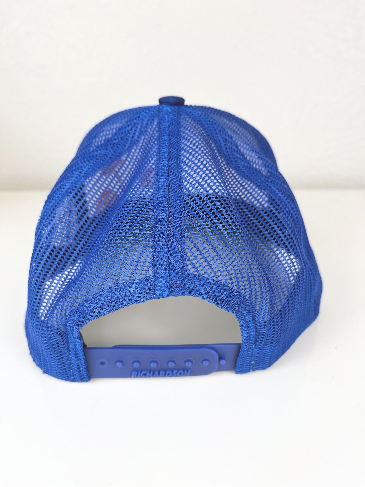 back view of a blue mesh hat with poppies hand embroidered on the front in coral outline and peach line fill, sitting on a white counter top