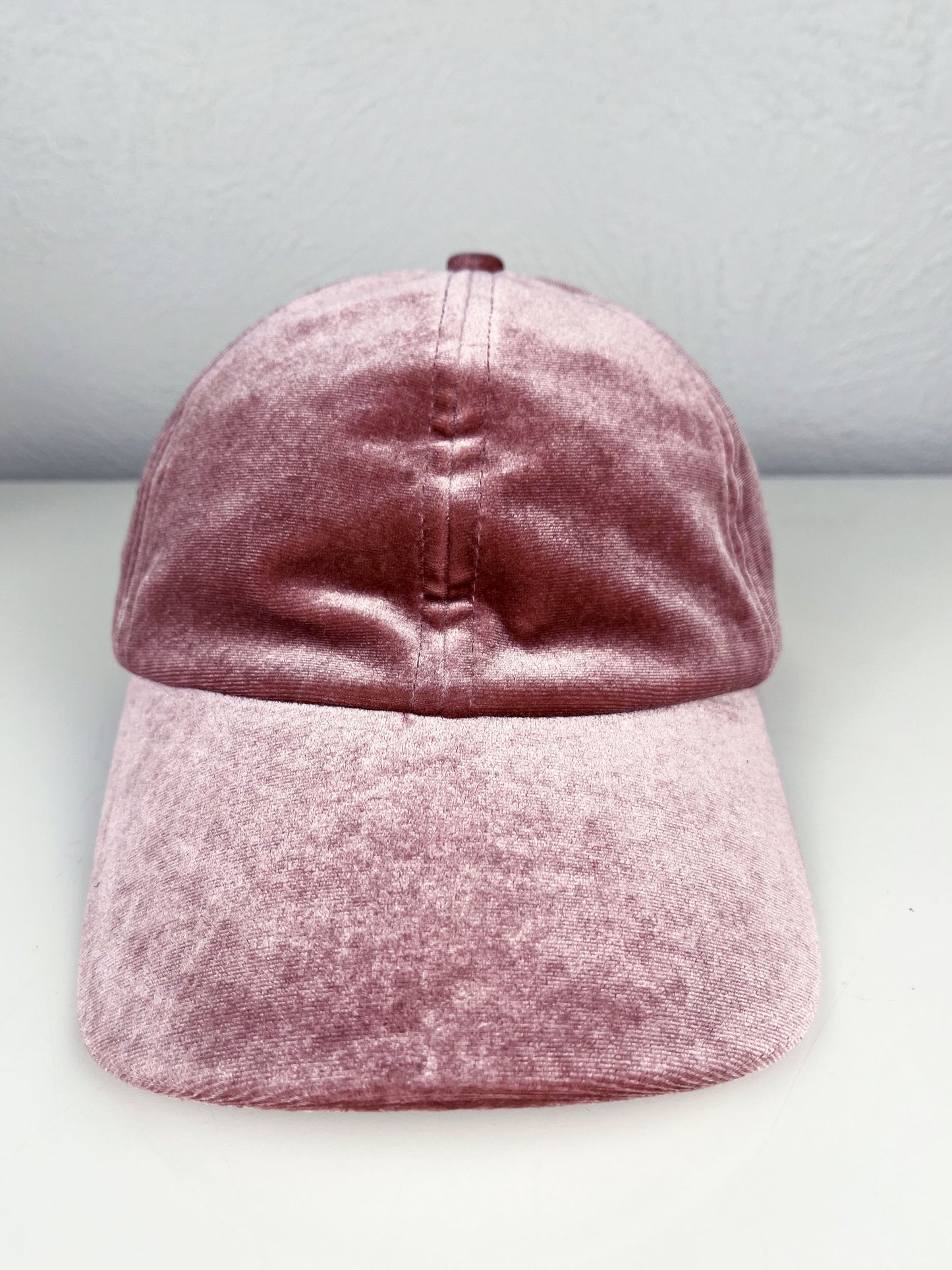 front view of a mauve velvet hat with dark mauve outline of a peony hand embroidered on the side, sitting on a white dresser