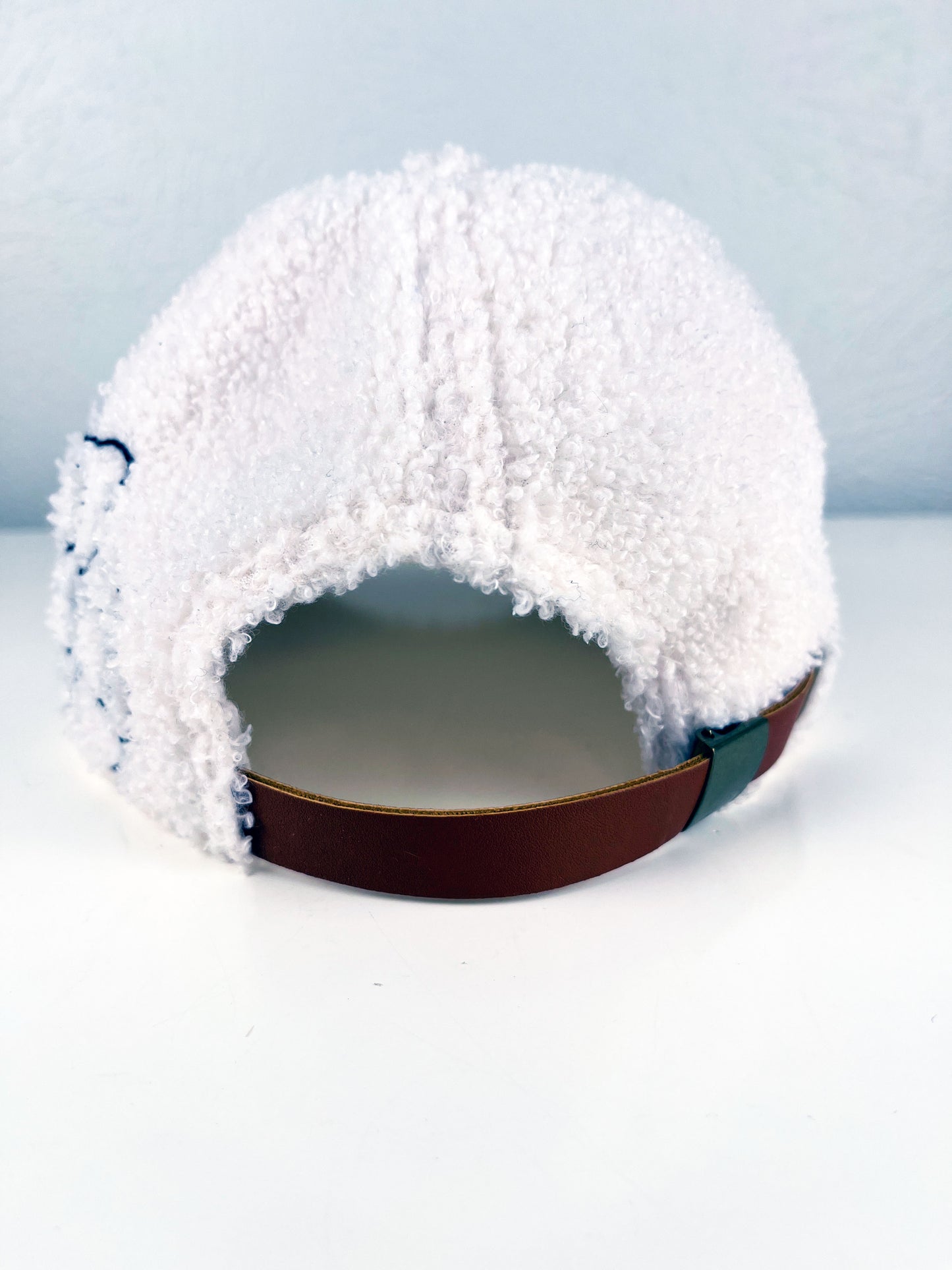 back view of a white boucle hat with black outline of a peony hand embroidered on the side, sitting on a white dresser