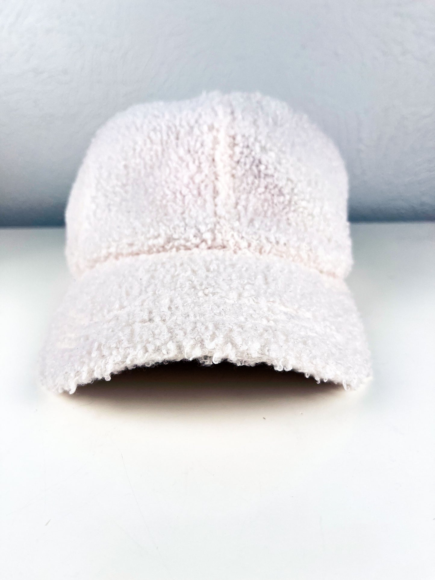 front view of a white boucle hat with black outline of a peony hand embroidered on the side, sitting on a white dresser