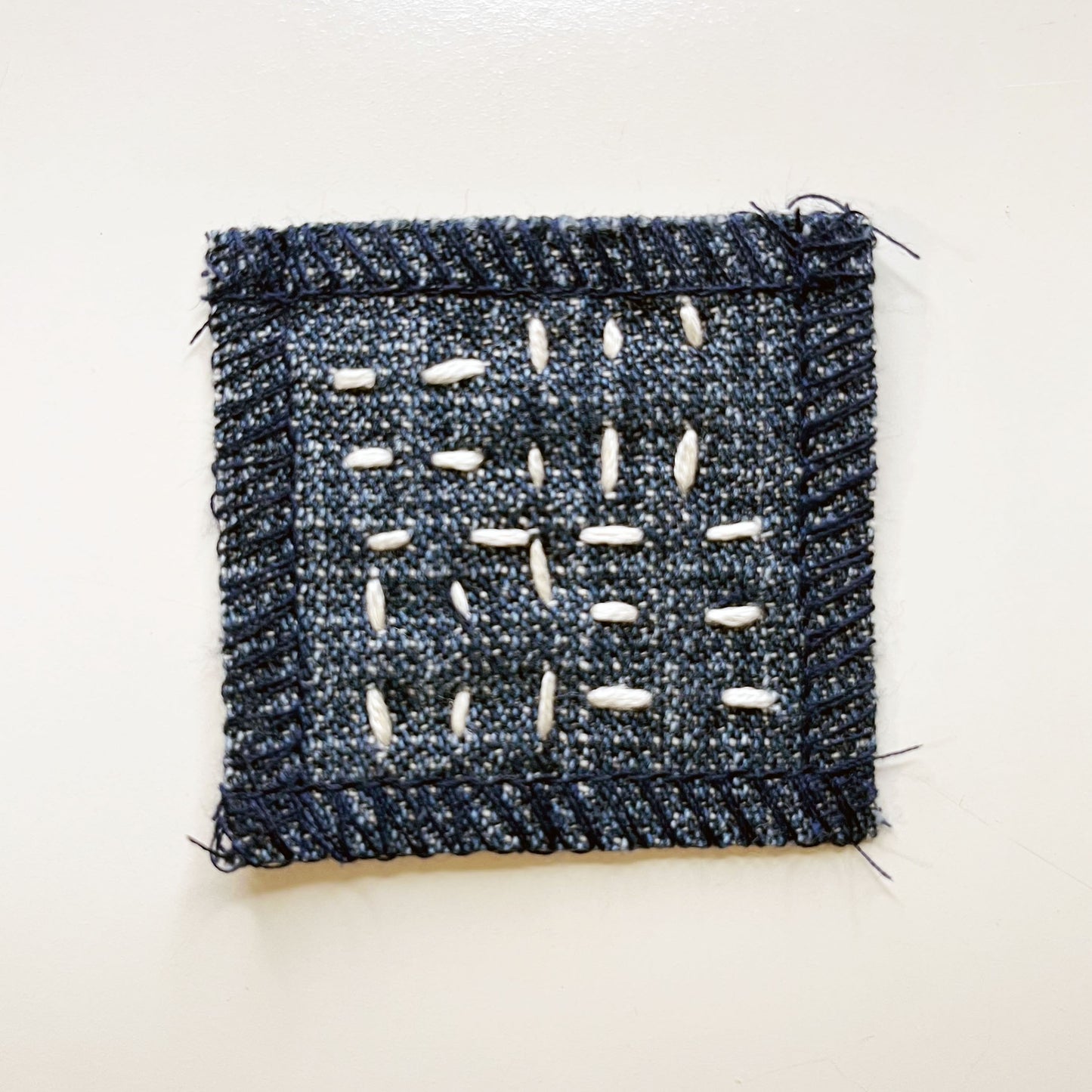 square denim patch with running stitches in a basketweave pattern on a white background
