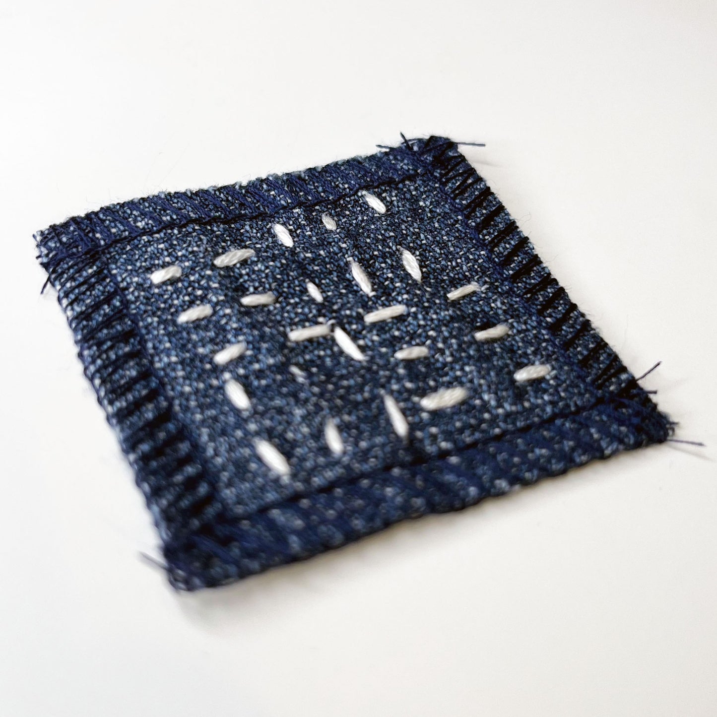 square denim patch with running stitches in a basketweave pattern on a white background