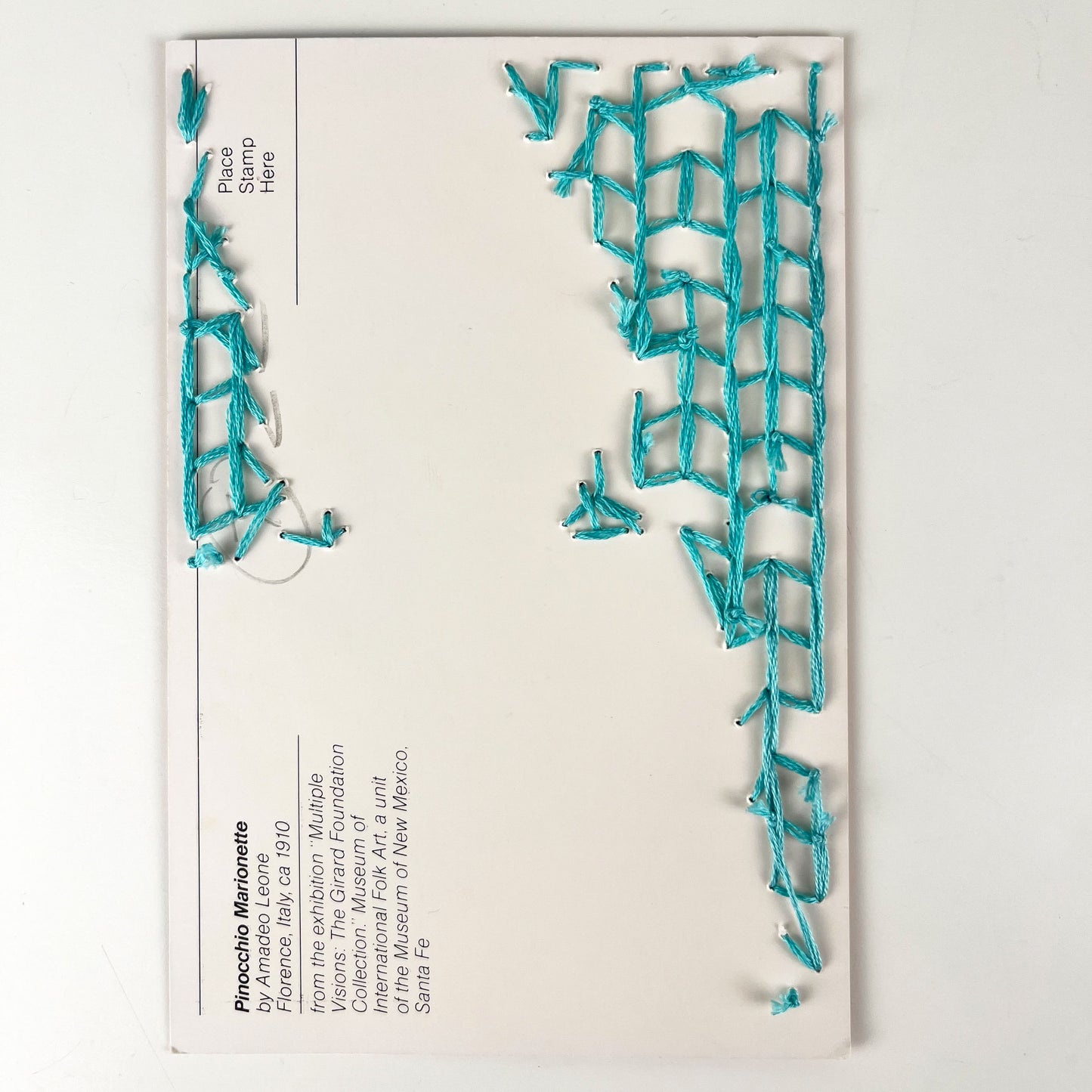 back side of a postcard, with the backside of a hand embroidered pattern in aqua, on a white background