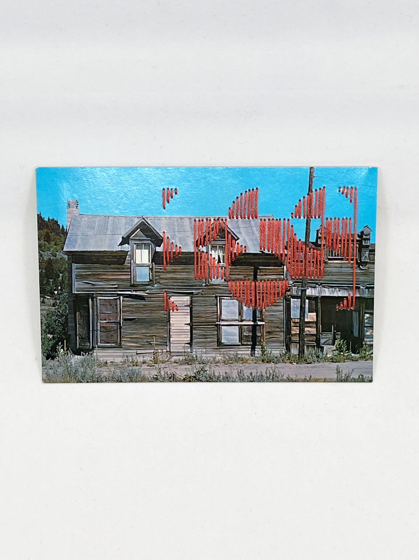postcard of an old building in Silver City Idaho stitched over in coral thread in a pattern of quarter circles in a grid of two by three