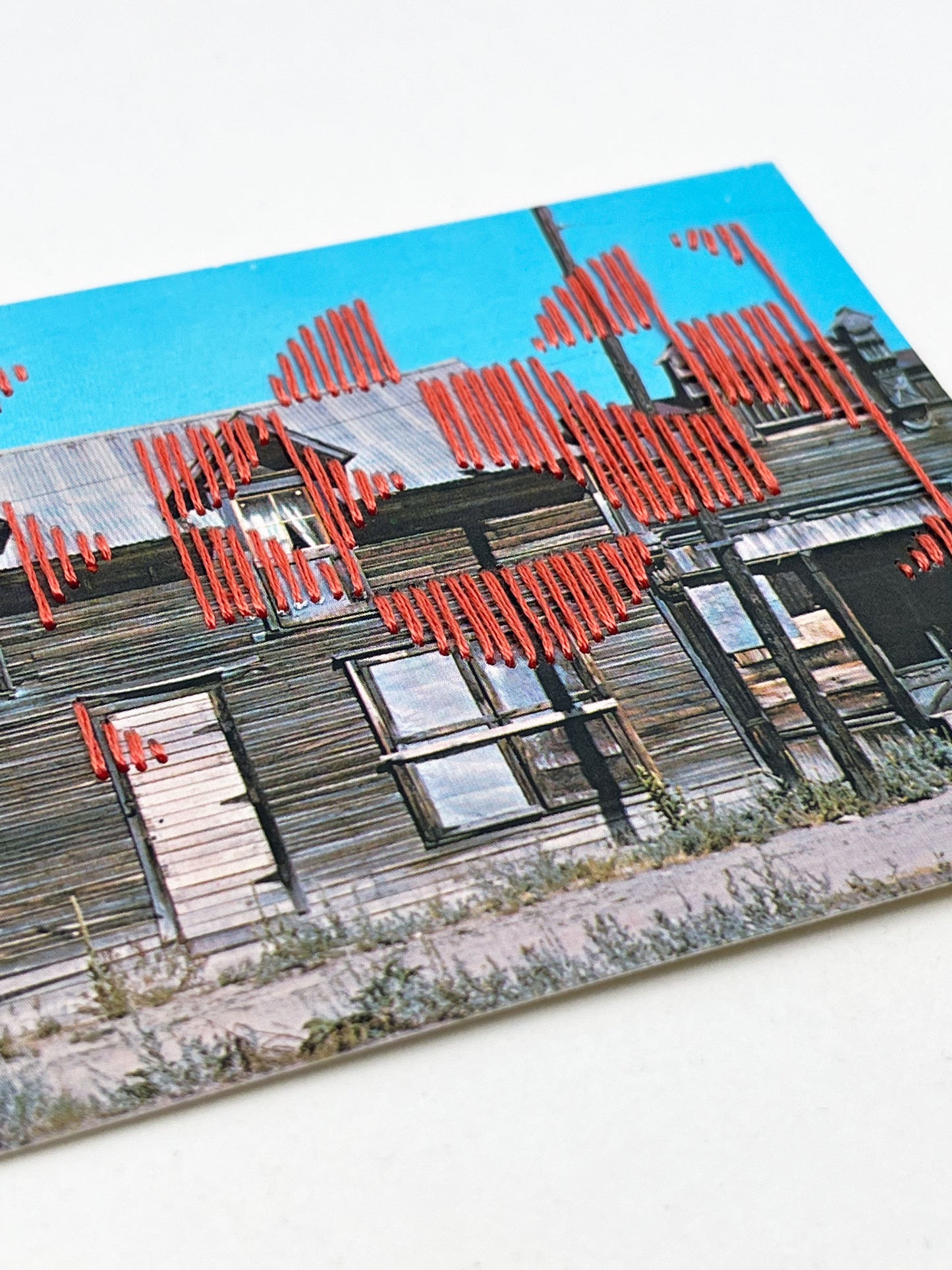postcard of an old building in Silver City Idaho stitched over in coral thread in a pattern of quarter circles in a grid of two by three