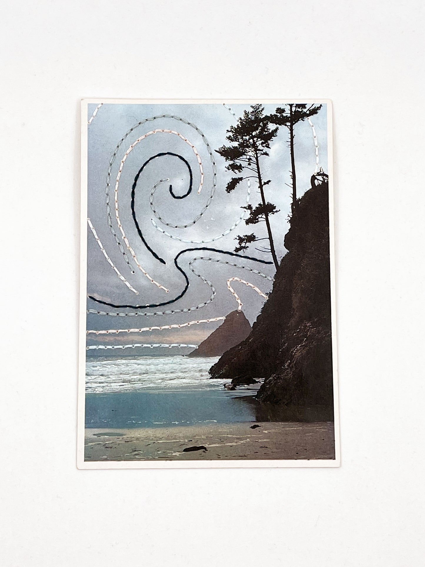 vintage postcard of the Oregon coast hand embroidered with swirls of forest green peach and grey in the sky