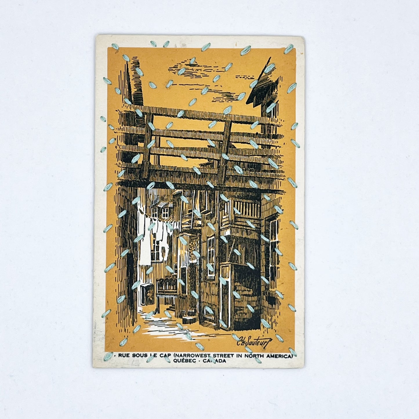 a golden yellow vintage postcard depicting a drawing of an alley in Quebec, stitched over with running stitches in light blue floss in a radiating X pattern