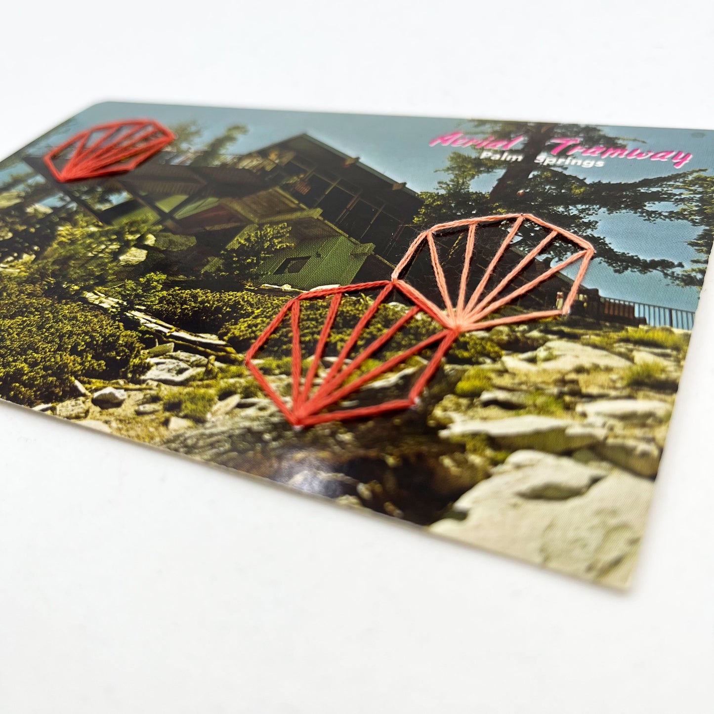 close up angled view of an old postcard of the Palm Springs Aerial Tramway, with coral hand embroidered art deco hexagons randomly placed on it