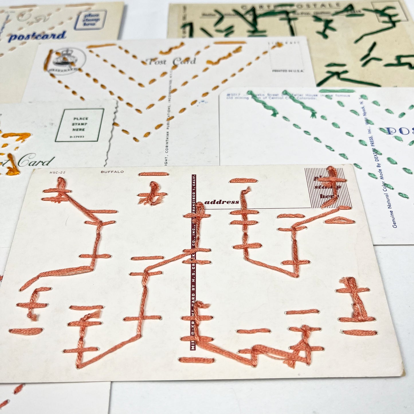 the back sides of a group of colorful vintage postcards hand stitched in corals and greens