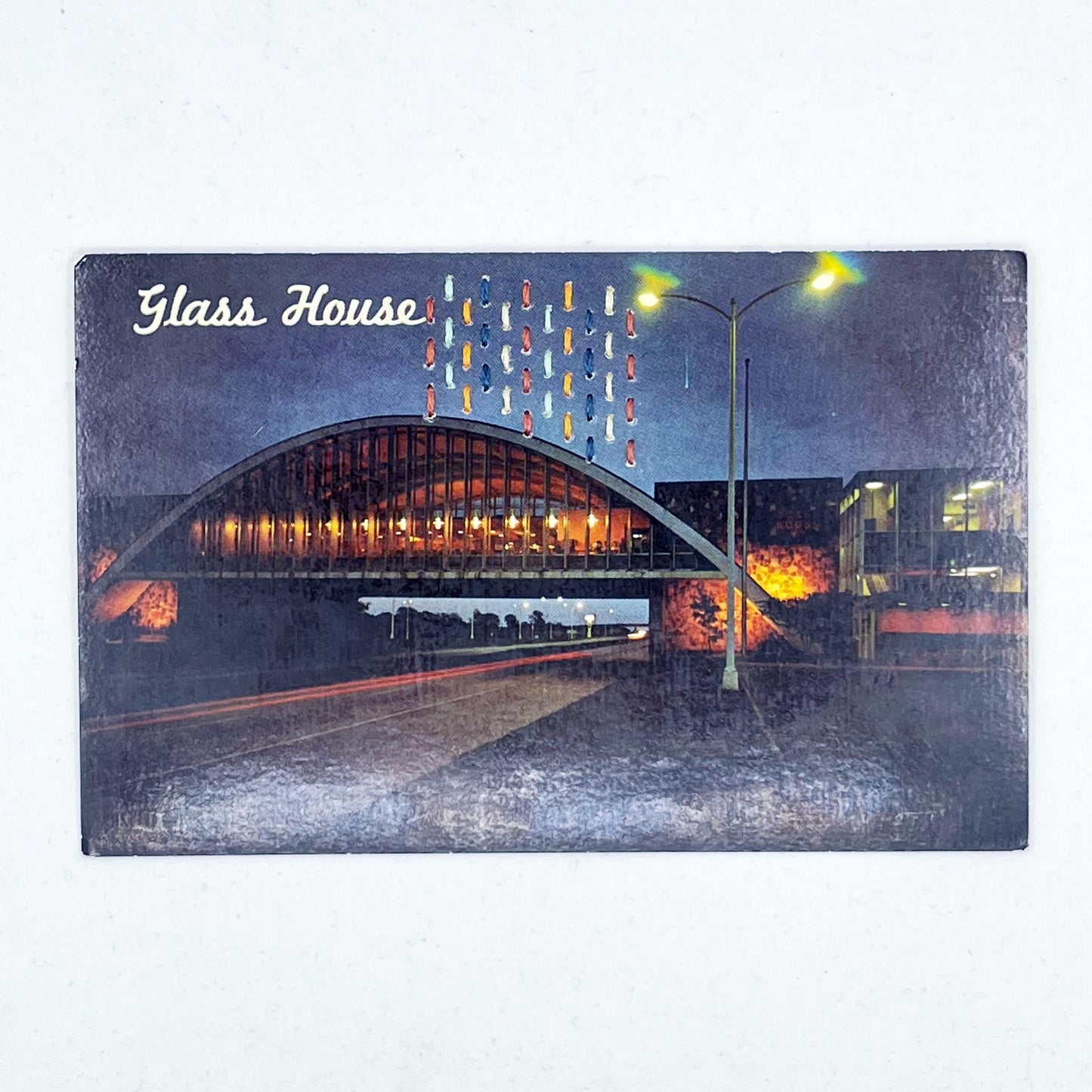 an old postcard of the Glass House rest stop restaurant, with multicolored hand embroidered lines in the sky, on a white surface