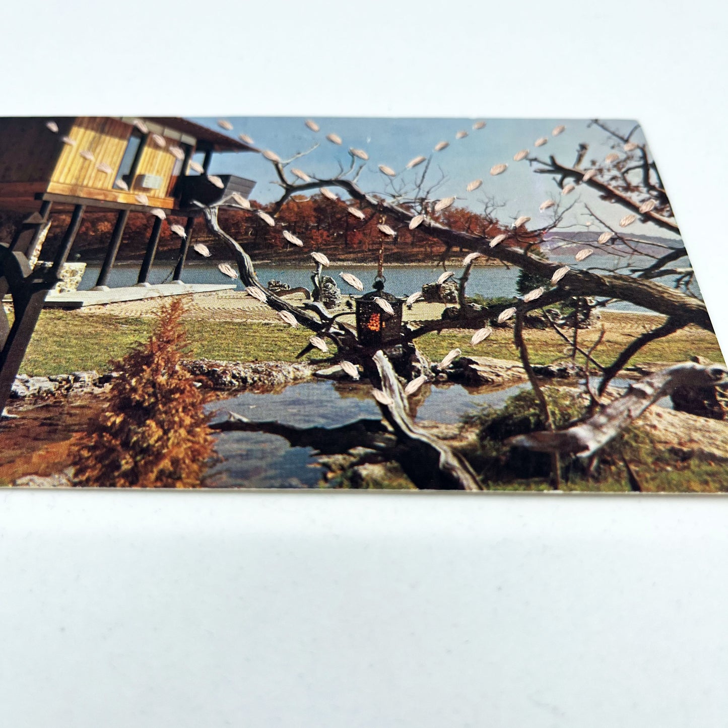 a vintage postcard of a Japanese inspired garden and house on a lake, hand stitched over with four rows of chevrons in running stitches with light pink thread, on a white background