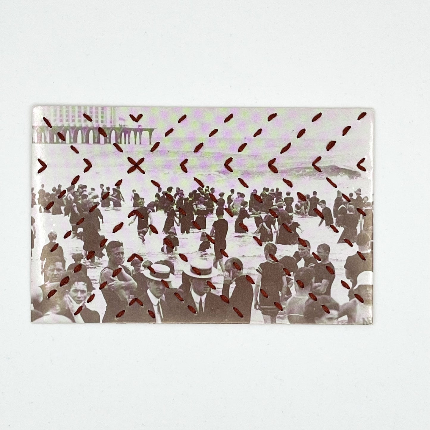 a vintage postcard of a crowd of people in the water in Atlantic City, hand stitched over with a radiating X pattern in brick red