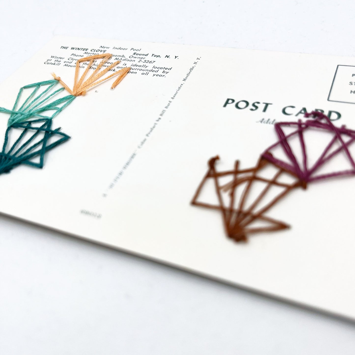 back side of a vintage postcard of an indoor pool, with art deco hexagons hand embroidered on it in aqua teal plum peach and brown