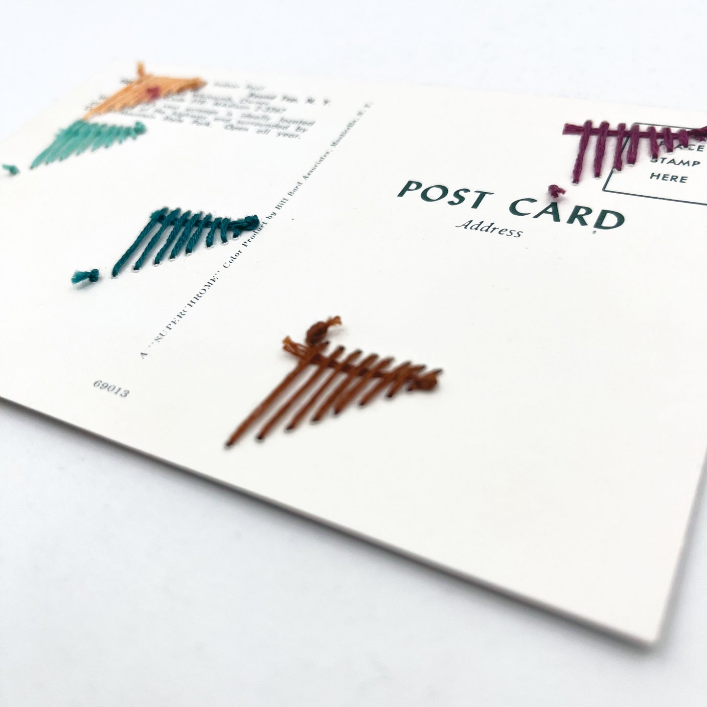 back side of a vintage postcard of an indoor pool, with randomly placed triangles hand embroidered on it in aqua teal plum peach and brown