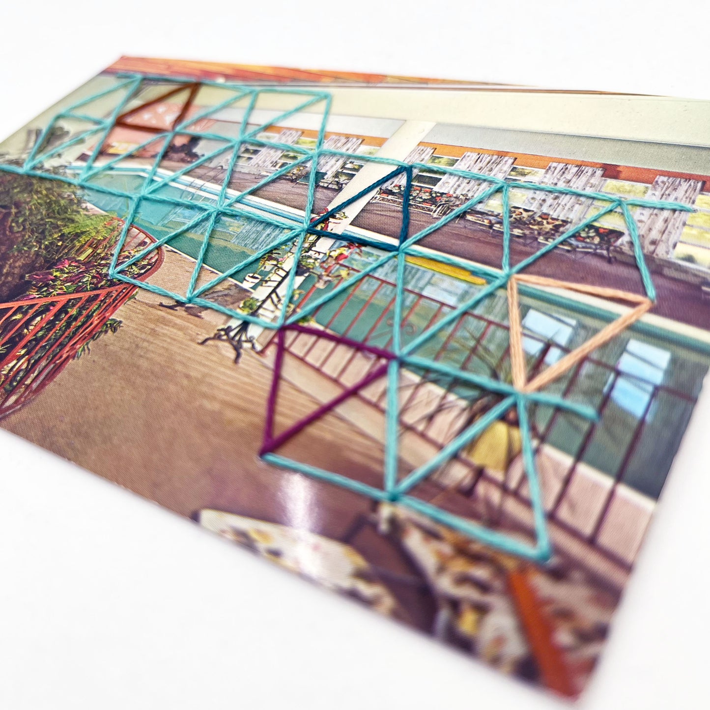 vintage postcard of an indoor pool, with a grid of triangles hand embroidered on it in aqua teal plum peach and brown
