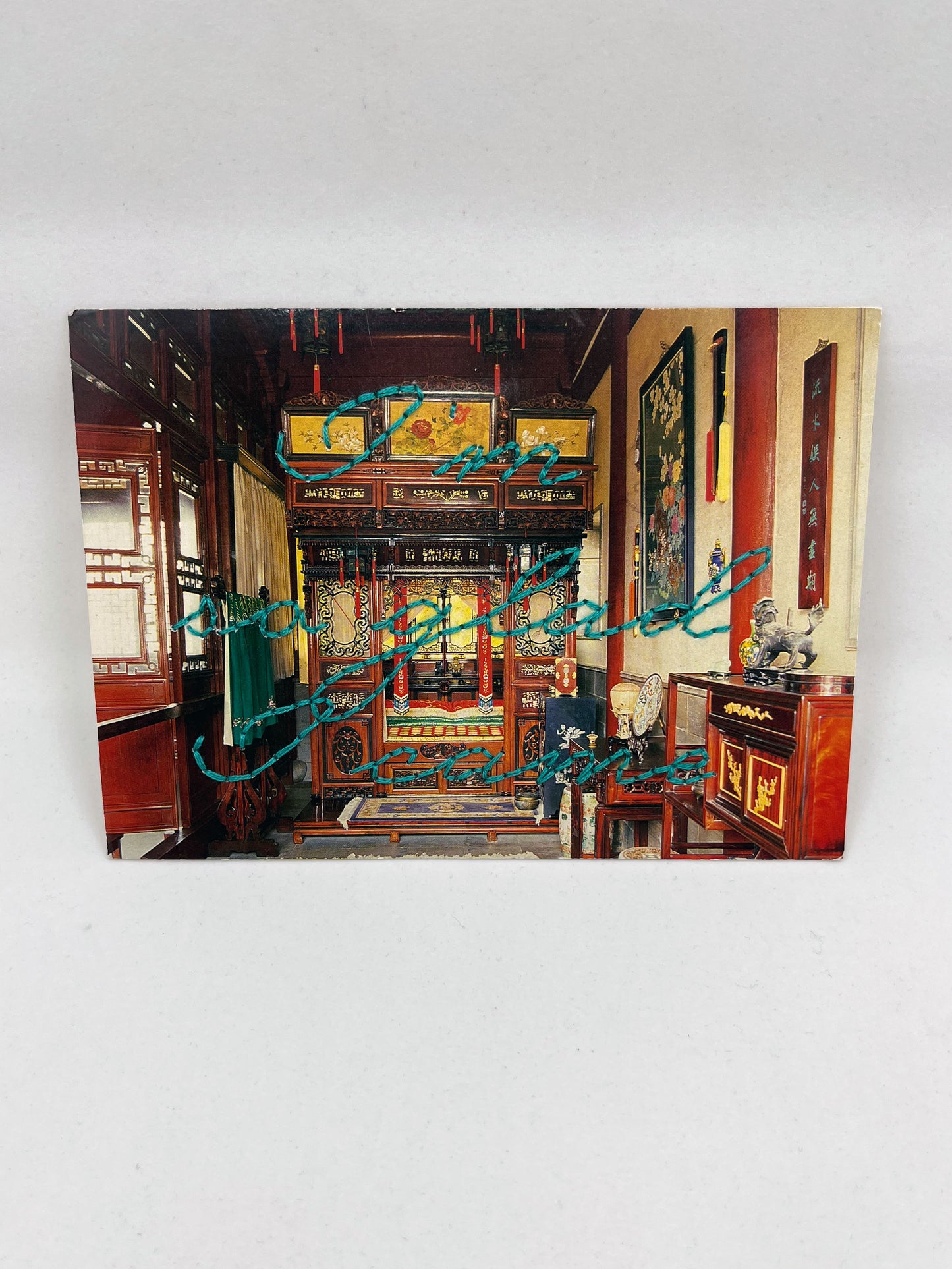 vintage postcard of an ornate Chinese bedroom, with the words I'm so glad I came hand embroidered in teal cursive backstitch over the top of it