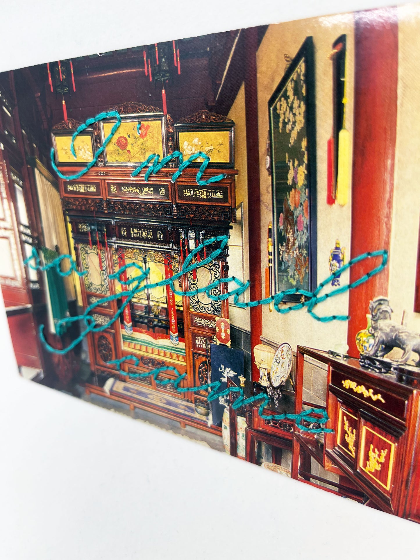 vintage postcard of an ornate Chinese bedroom, with the words I'm so glad I came hand embroidered in teal cursive backstitch over the top of it