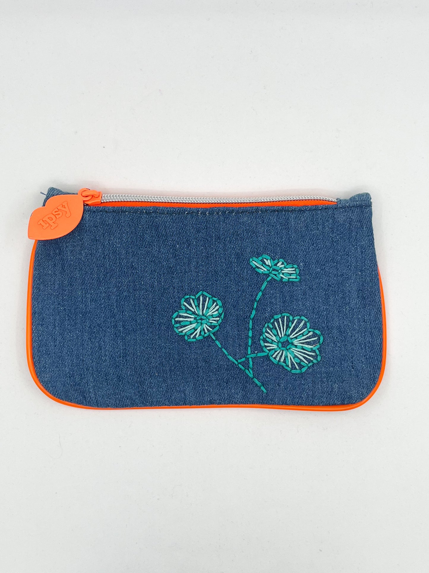denim Ipsy zip pouch with neon orange piping and zipper, hand embroidered with aqua poppies on a white background