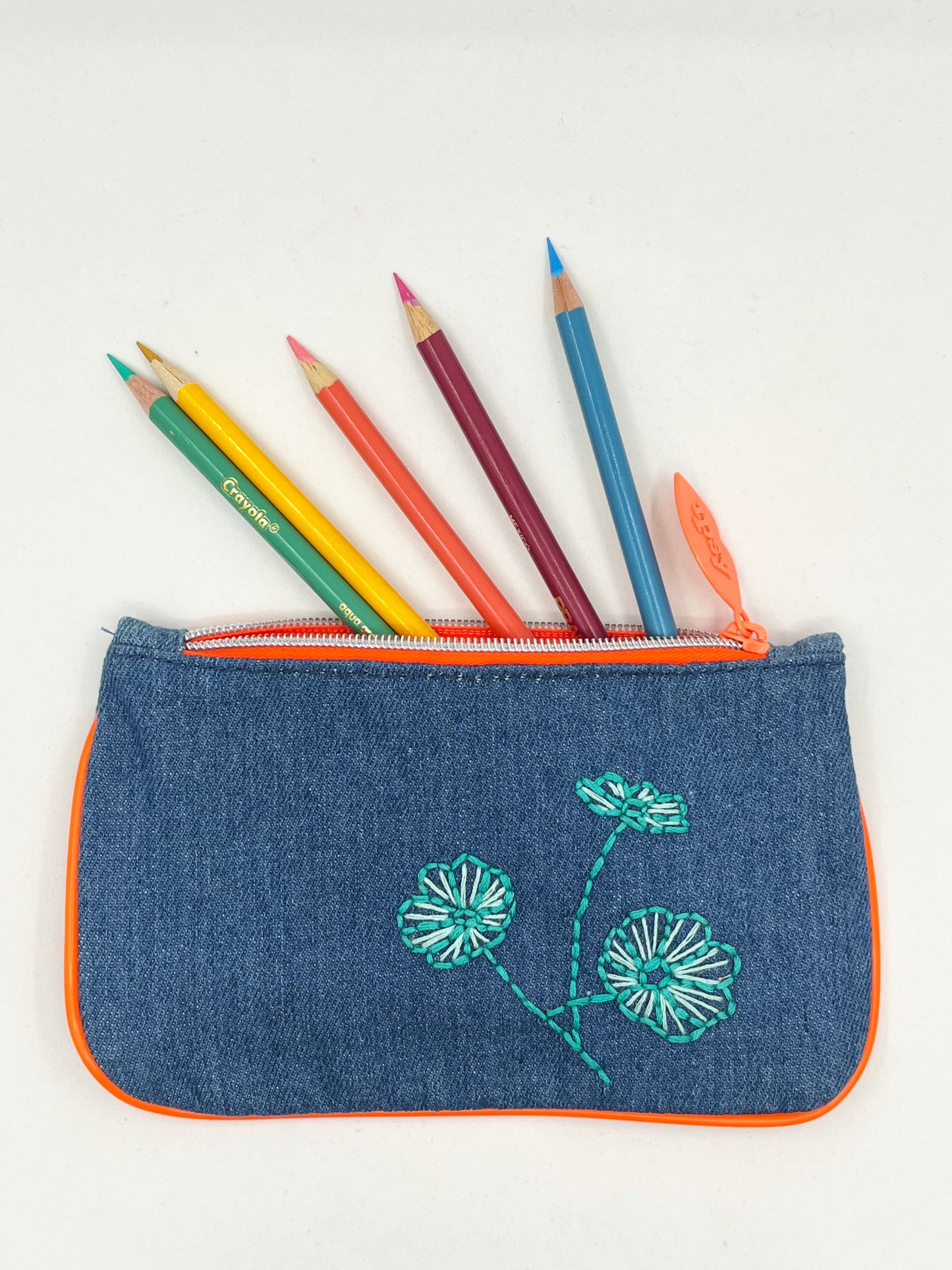 denim Ipsy zip pouch with neon orange piping and zipper, hand embroidered with aqua poppies with pencils coming out of the top of it