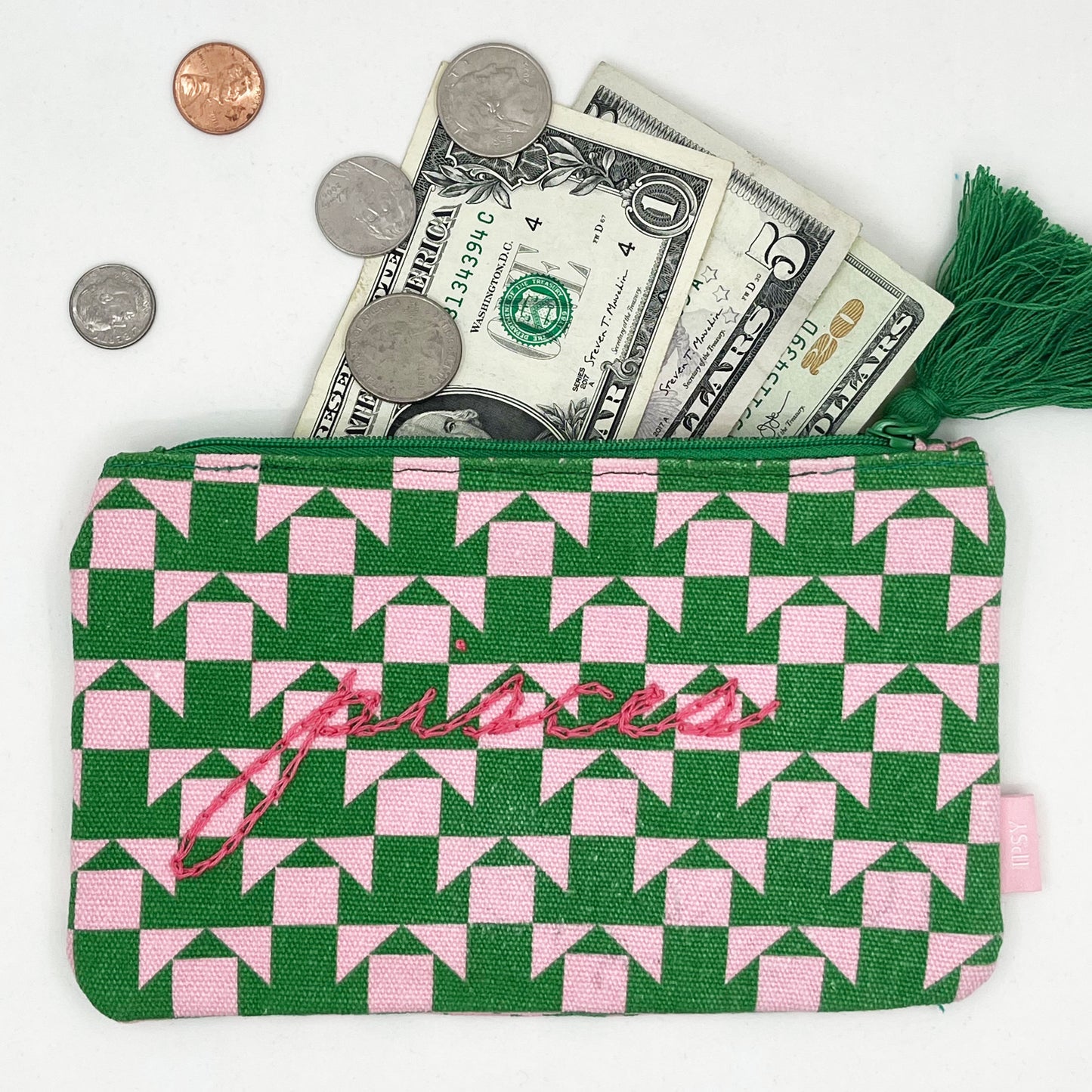 zip pouch with a pink and green geometric design on it hand embroidered in hot pink with the word pisces in chainstitch with money spilling out the top of it