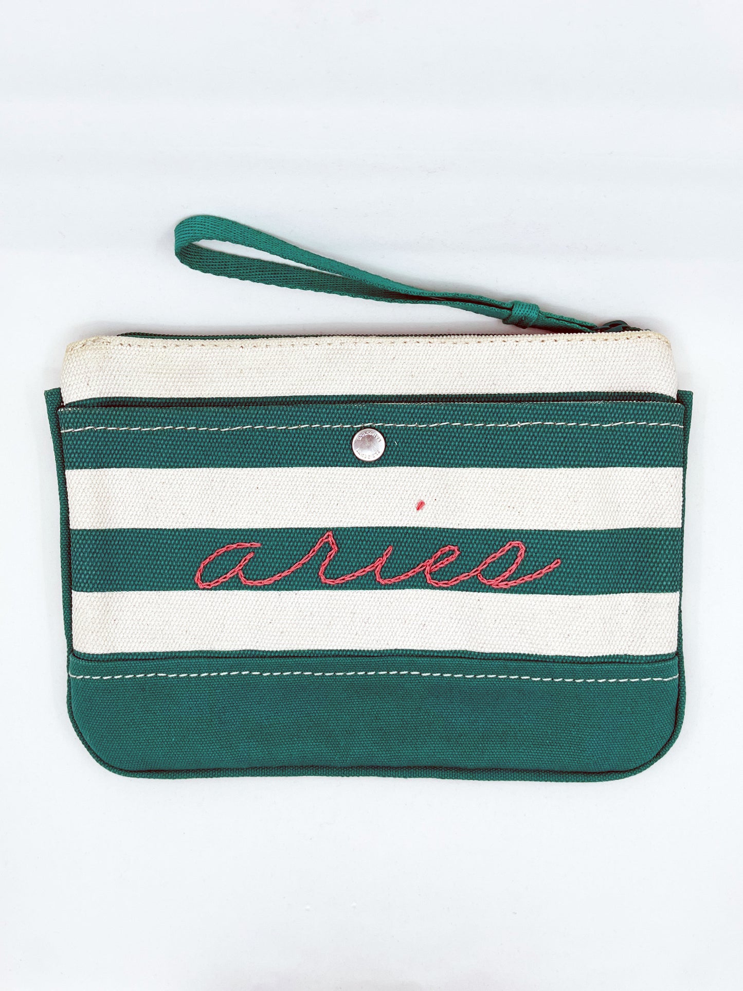 green and cream zipper wristlet with the word aries hand embroidered on it in coral chainstitch