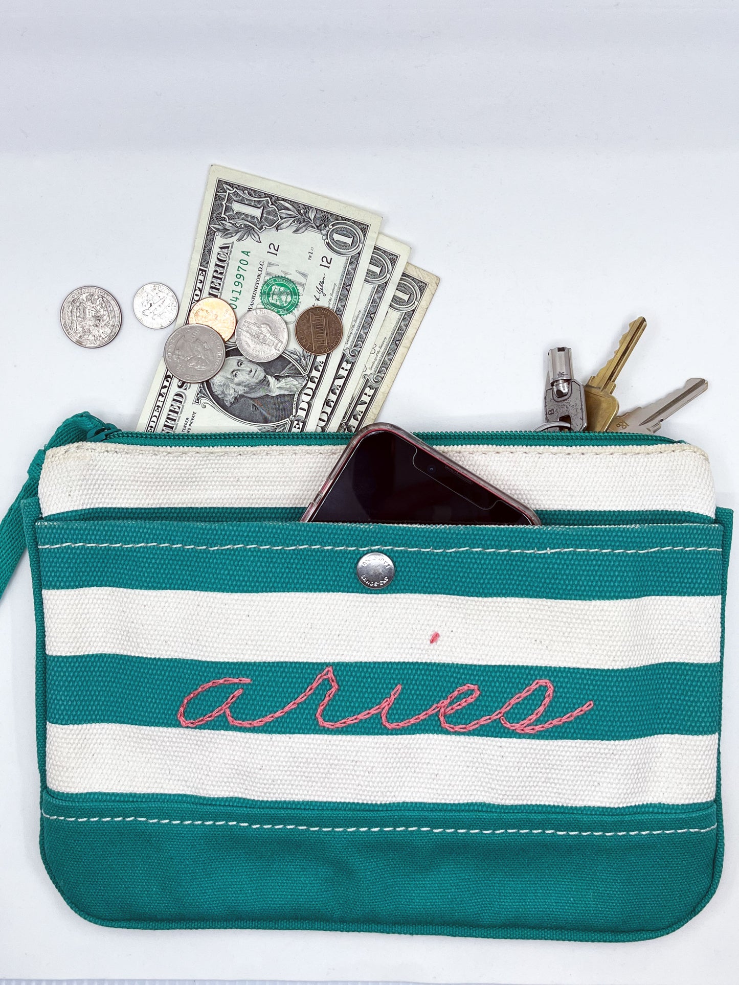 green and cream zipper wristlet with the word aries hand embroidered on it in coral chainstitch with money keys and a phone coming out of the top of it
