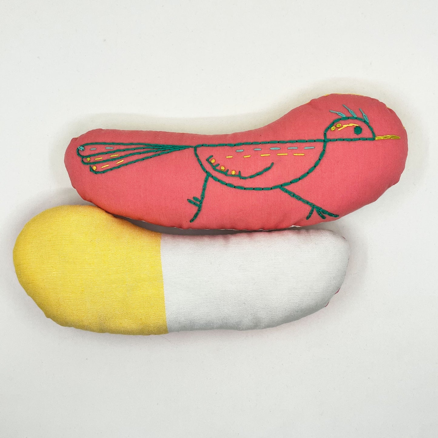 colorfully hand embroidered stuffed pillow animal of a roadrunner on coral fabric, behind it one turned around showing the back side made of shite and yellow color blocked fabric