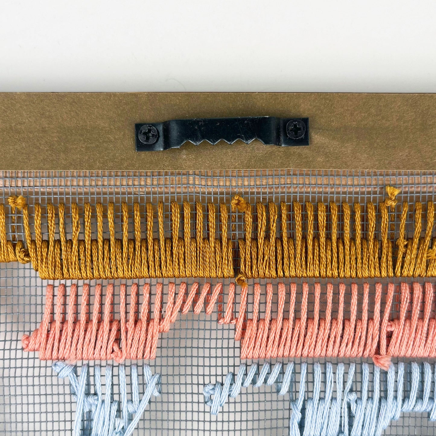back view of a frame edge with a sawtooth hanger on it, backside of hand stitched window screen show below it