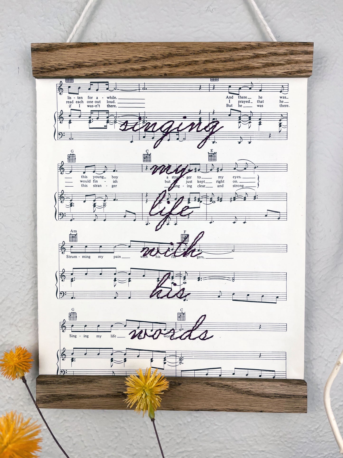 sheet music for the song Killing Me Softly With His Words hanging in a magnetic wood frame with the words singing my life with his words hand embroidered over it in eggplant colored thread in cursive