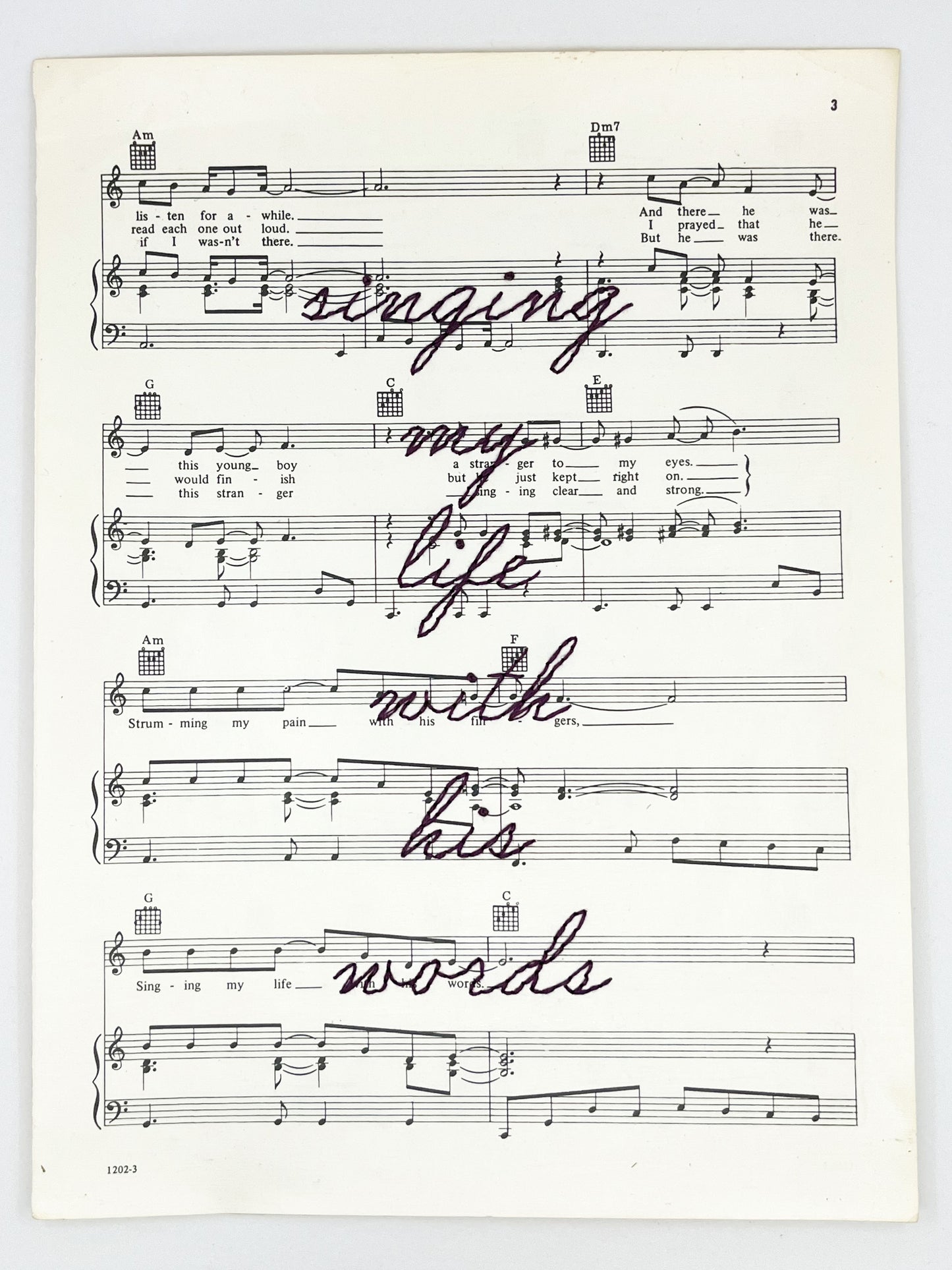 sheet music for the song Killing Me Softly With His Words with the words singing my life with his words hand embroidered over it in eggplant colored thread in cursive, on a white background