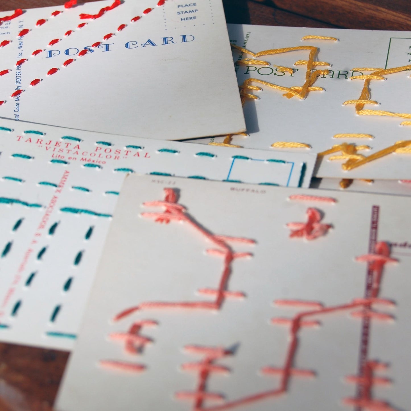 the back sides of a group of colorful vintage postcards hand stitched in yellow, red, aqua and coral