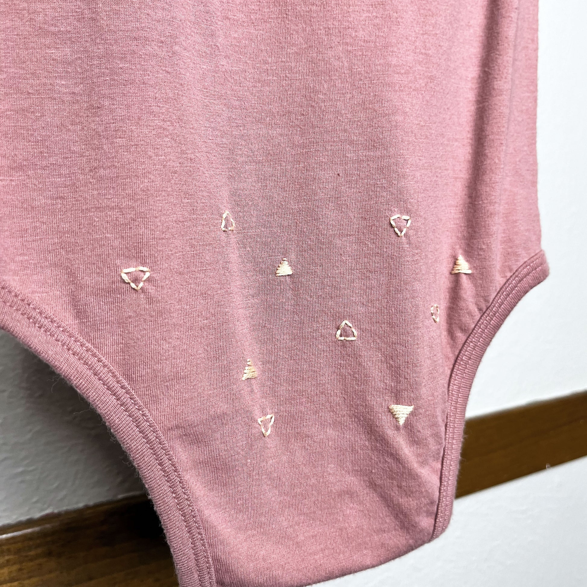 Close up view of a mauve baby one piece,  with small peach triangle stitches scattered over the bum