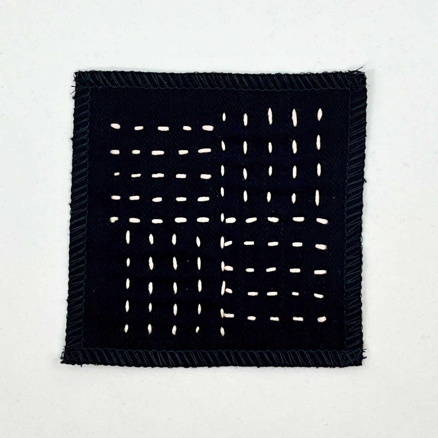 a square black denim patch hand stitched in peach with sashiko style running stitches in the pattern of a basket weave on a white background
