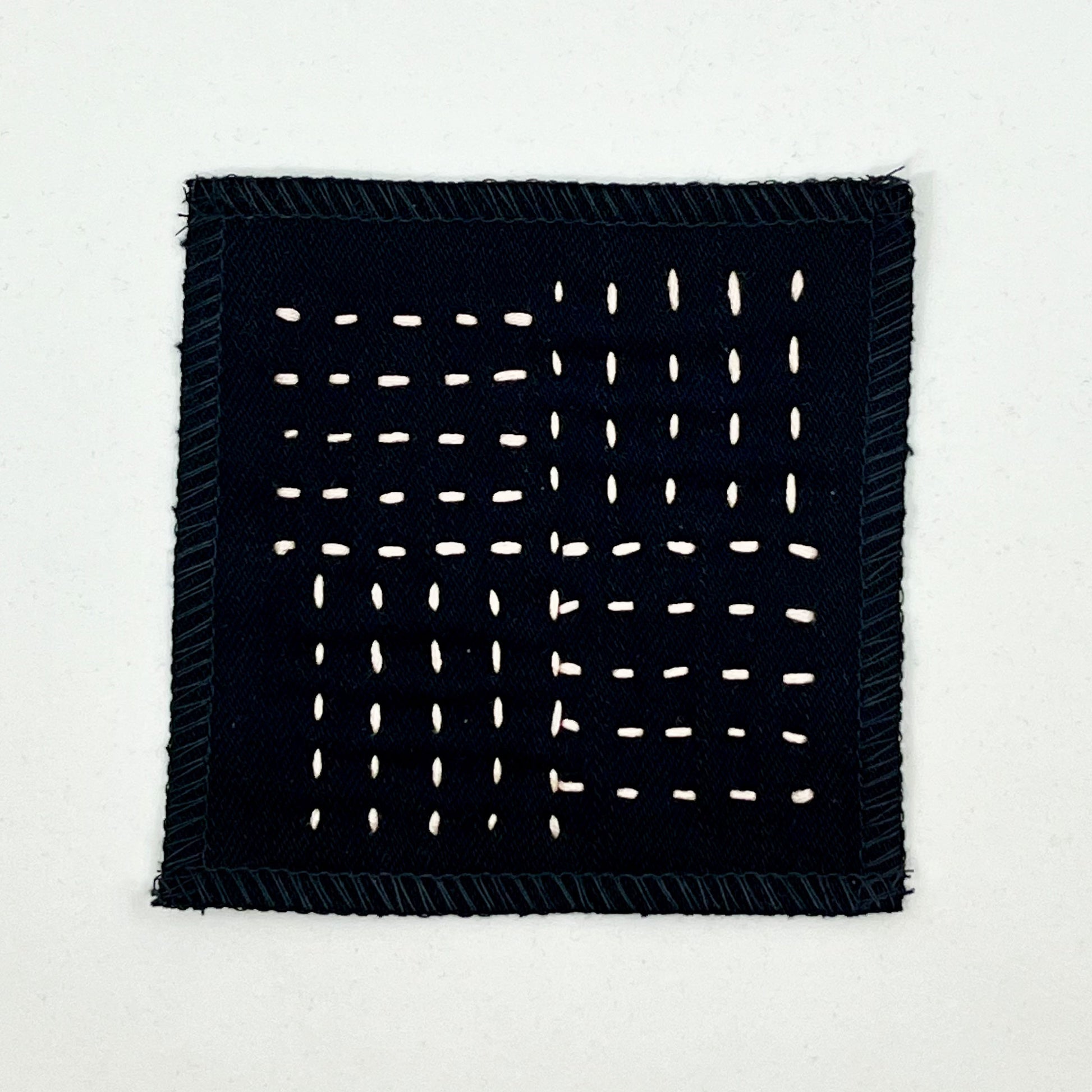 a square black denim patch hand stitched in peach with sashiko style running stitches in the pattern of a basket weave on a white background