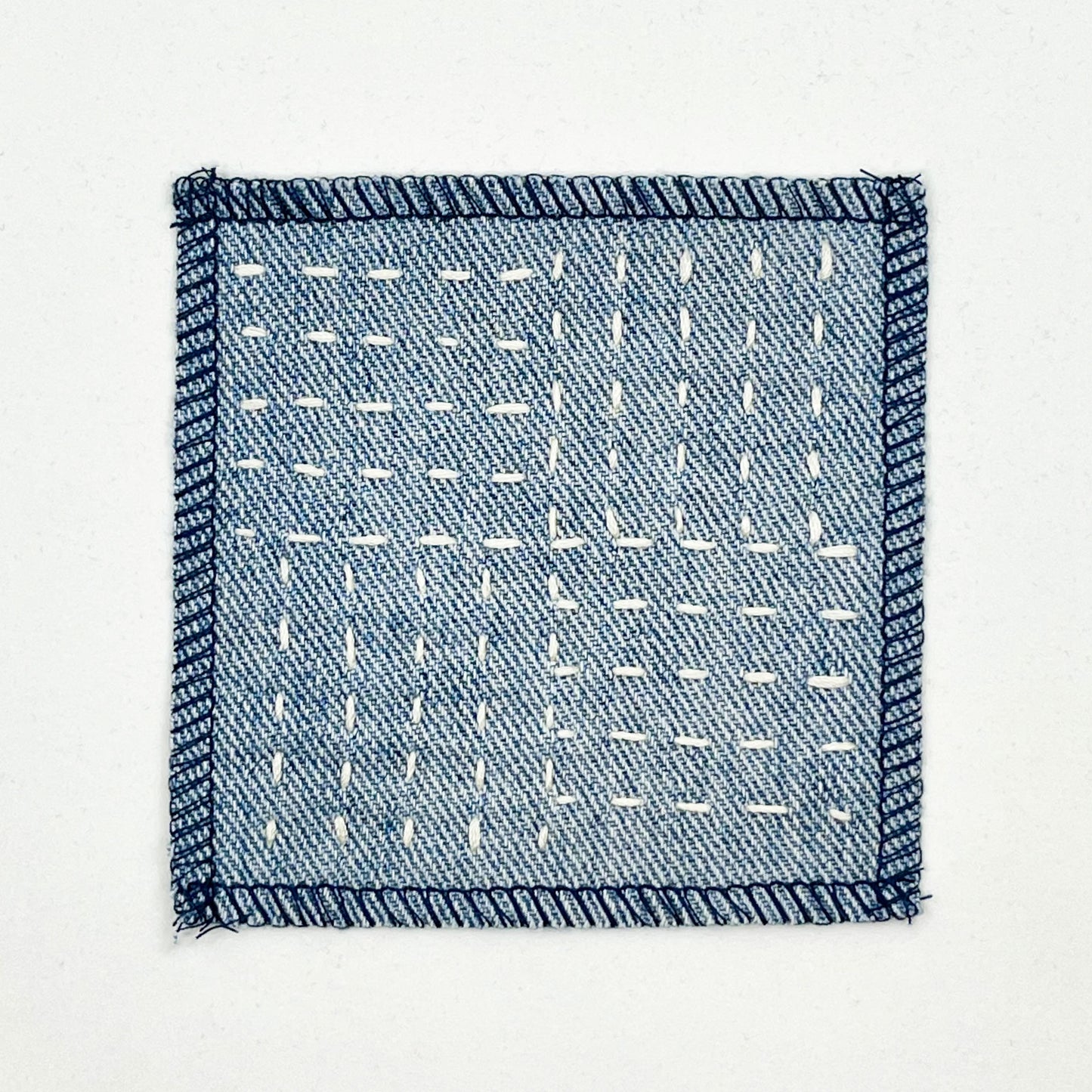 a square denim patch hand stitched in ivory with sashiko style running stitches in the pattern of a basket weave on a white background