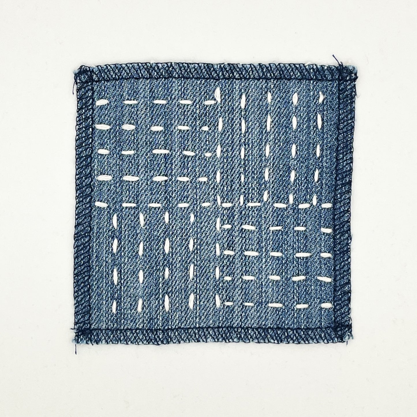 a square denim patch hand stitched in ivory with sashiko style running stitches in the pattern of a basket weave on a white background