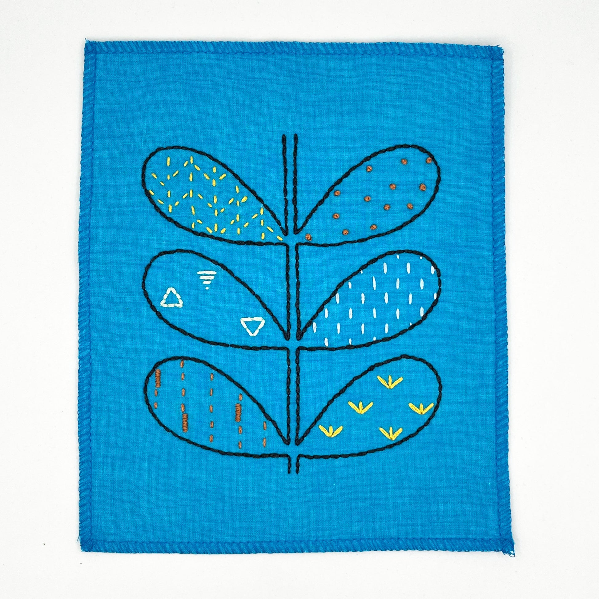 small bright blue fabric wall hangings, hand embroidered with the outline of symmetrical petals on a stem in navy, each petal filled with different stitches like french knots, running stitches and triangles, in different colors, on a white background