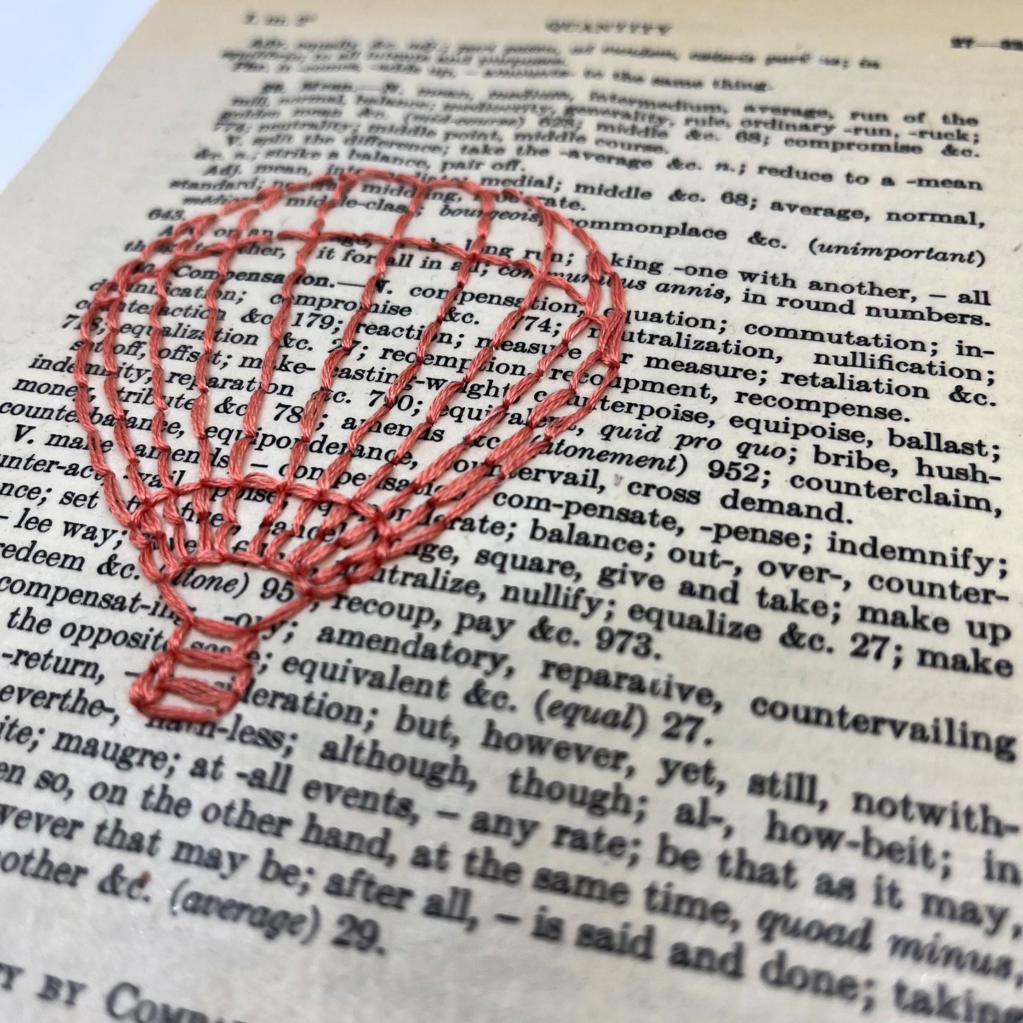 a close up angled view of a vintage thesaurus page, hand stitched over with an outline of a hot air balloon in coral thread