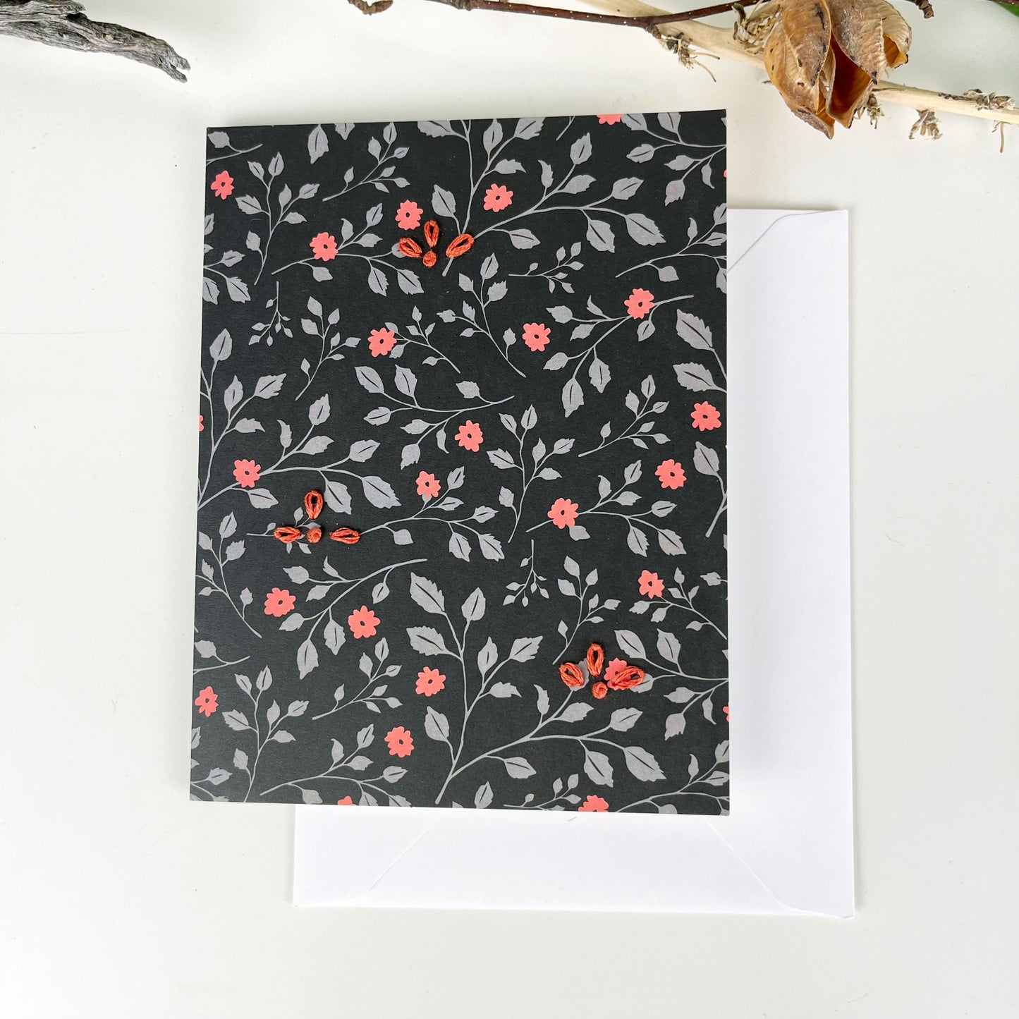 black floral greeting card embellished with small hand embroidered flowers on a white counter