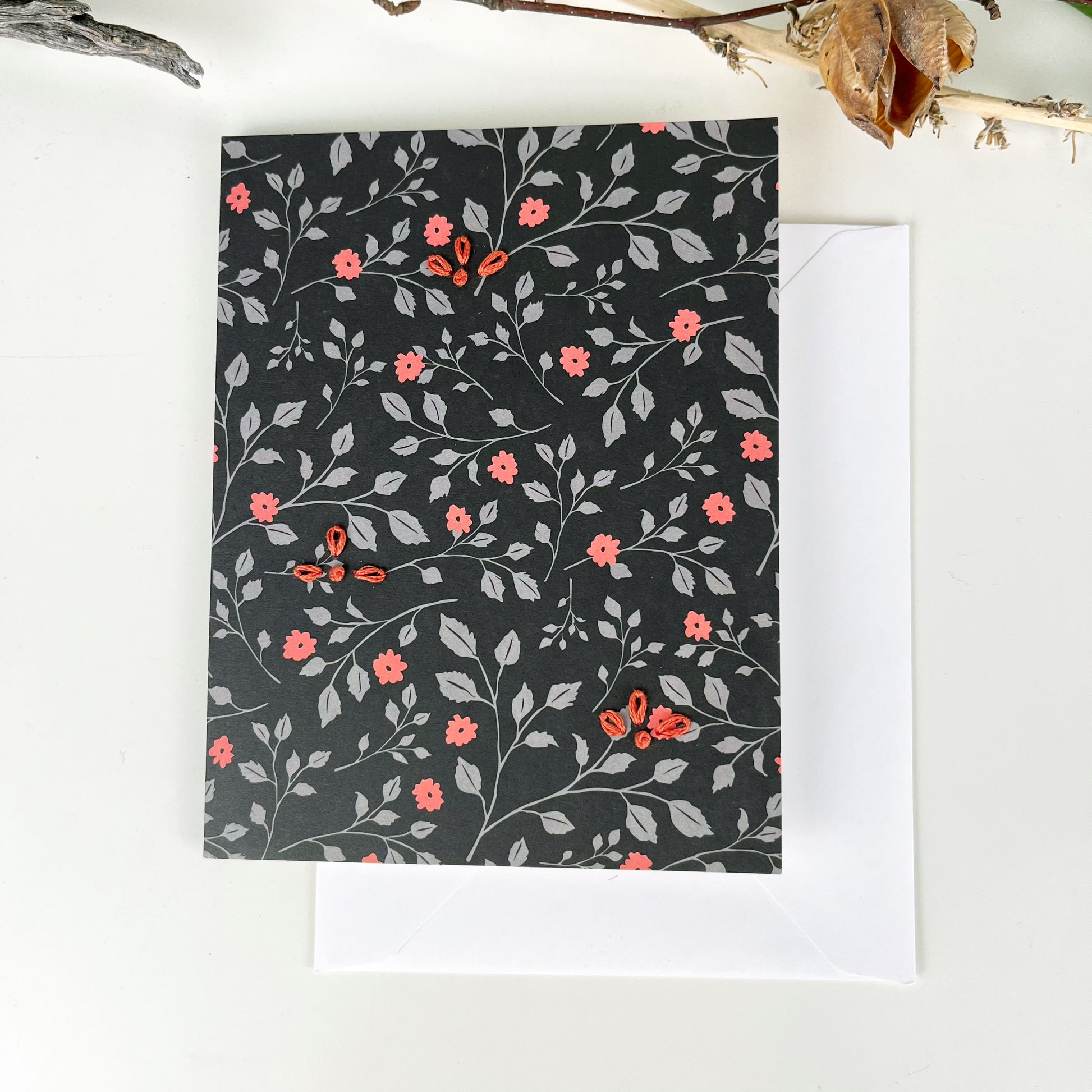 black floral greeting card embellished with small hand embroidered flowers on a white counter