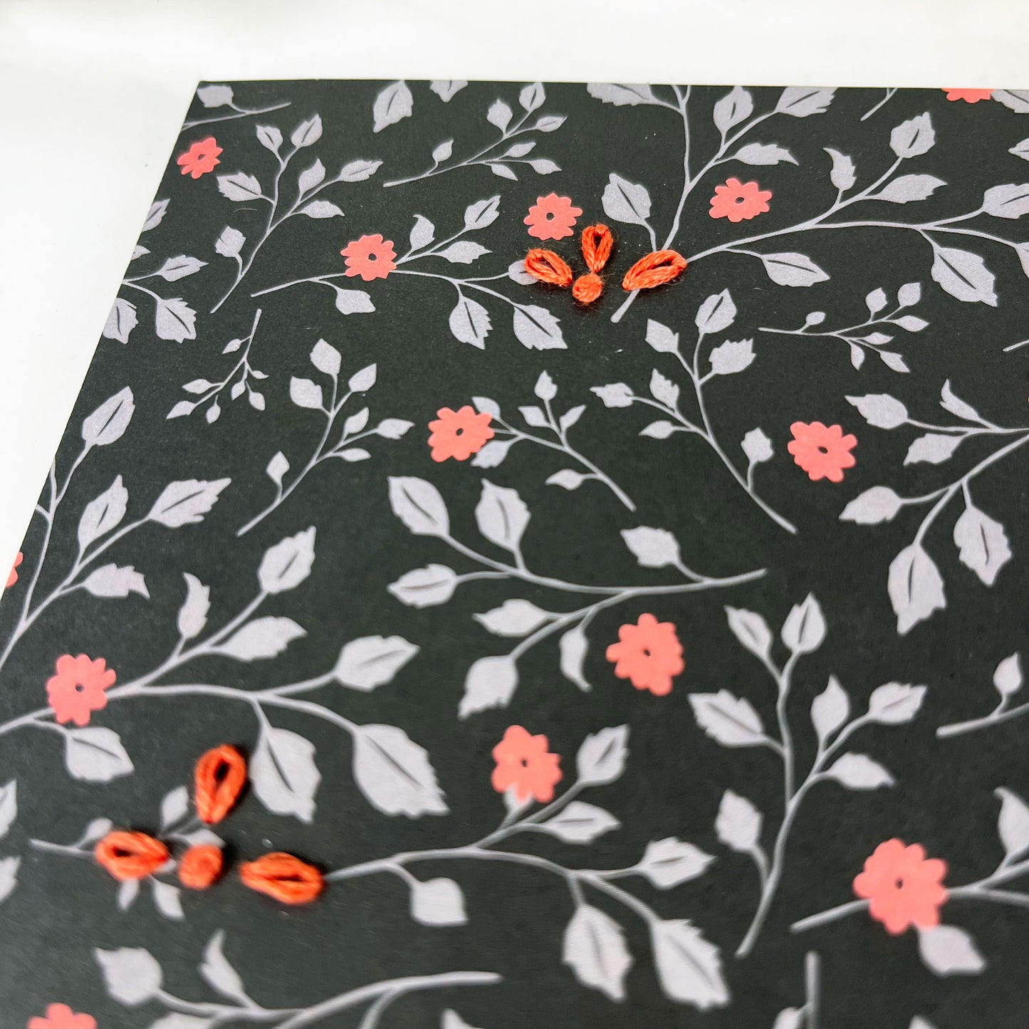 black floral greeting card embellished with small hand embroidered flowers on a white counter