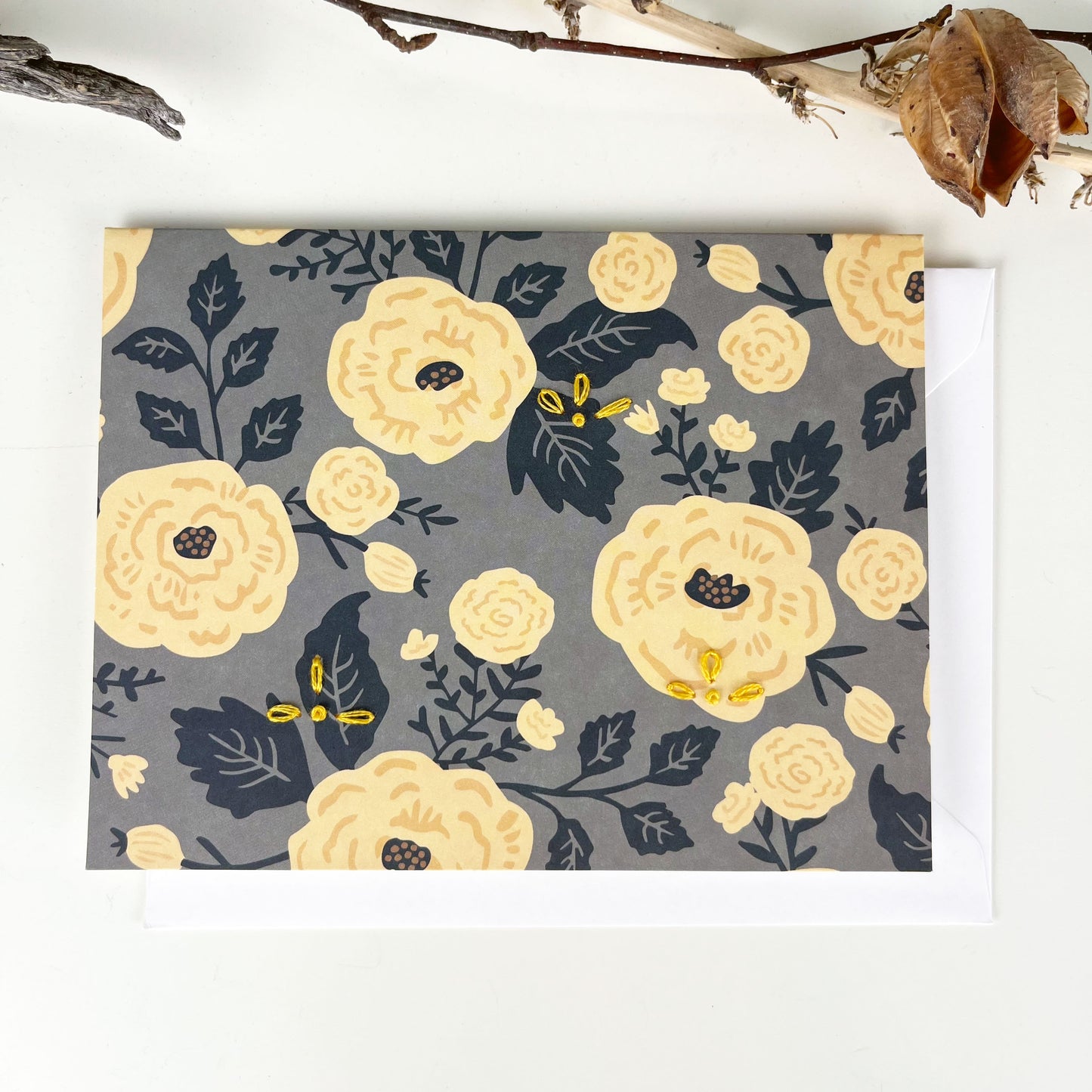 gray and yellow floral greeting card embellished with small hand embroidered flowers on a white counter