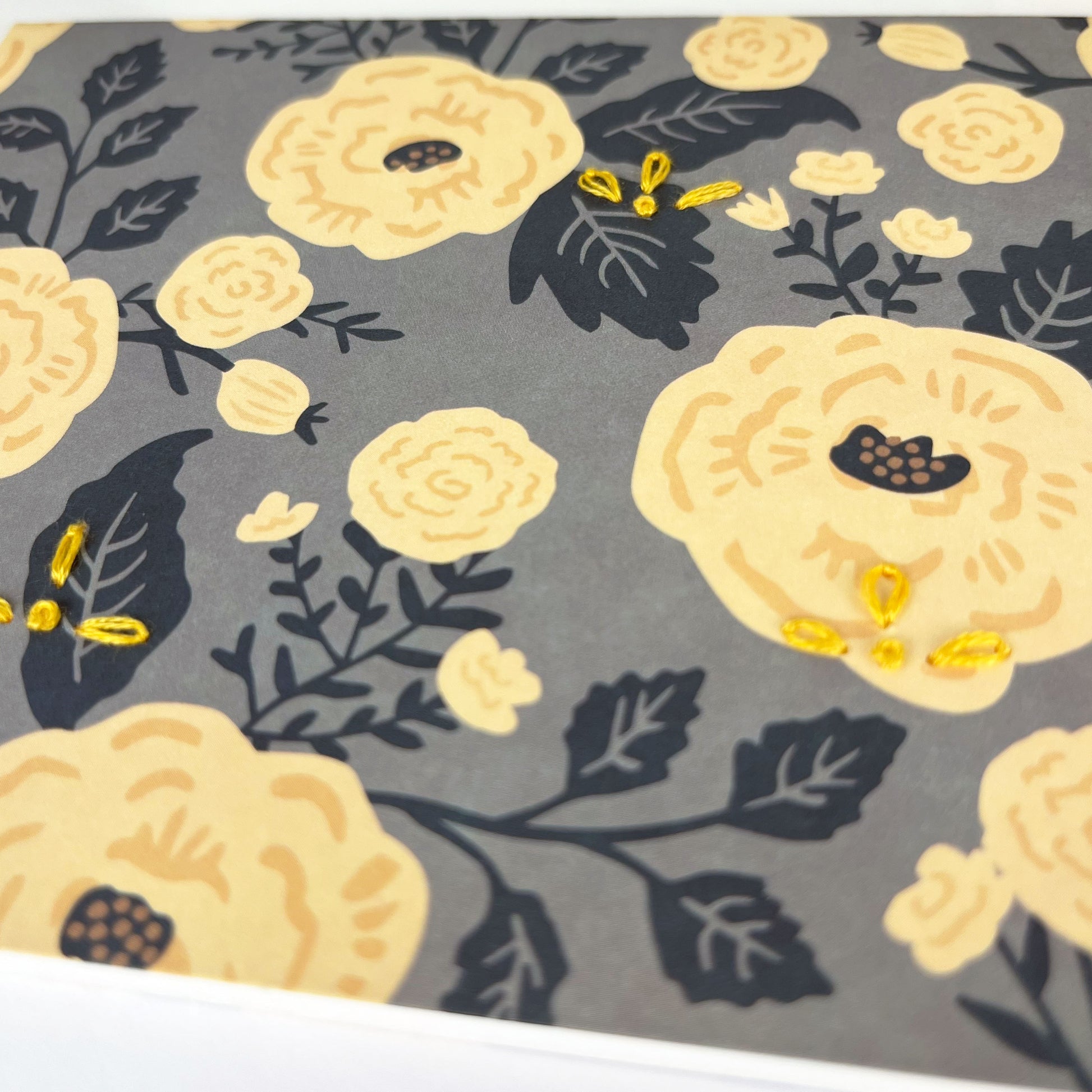 gray and yellow floral greeting card embellished with small hand embroidered flowers on a white counter