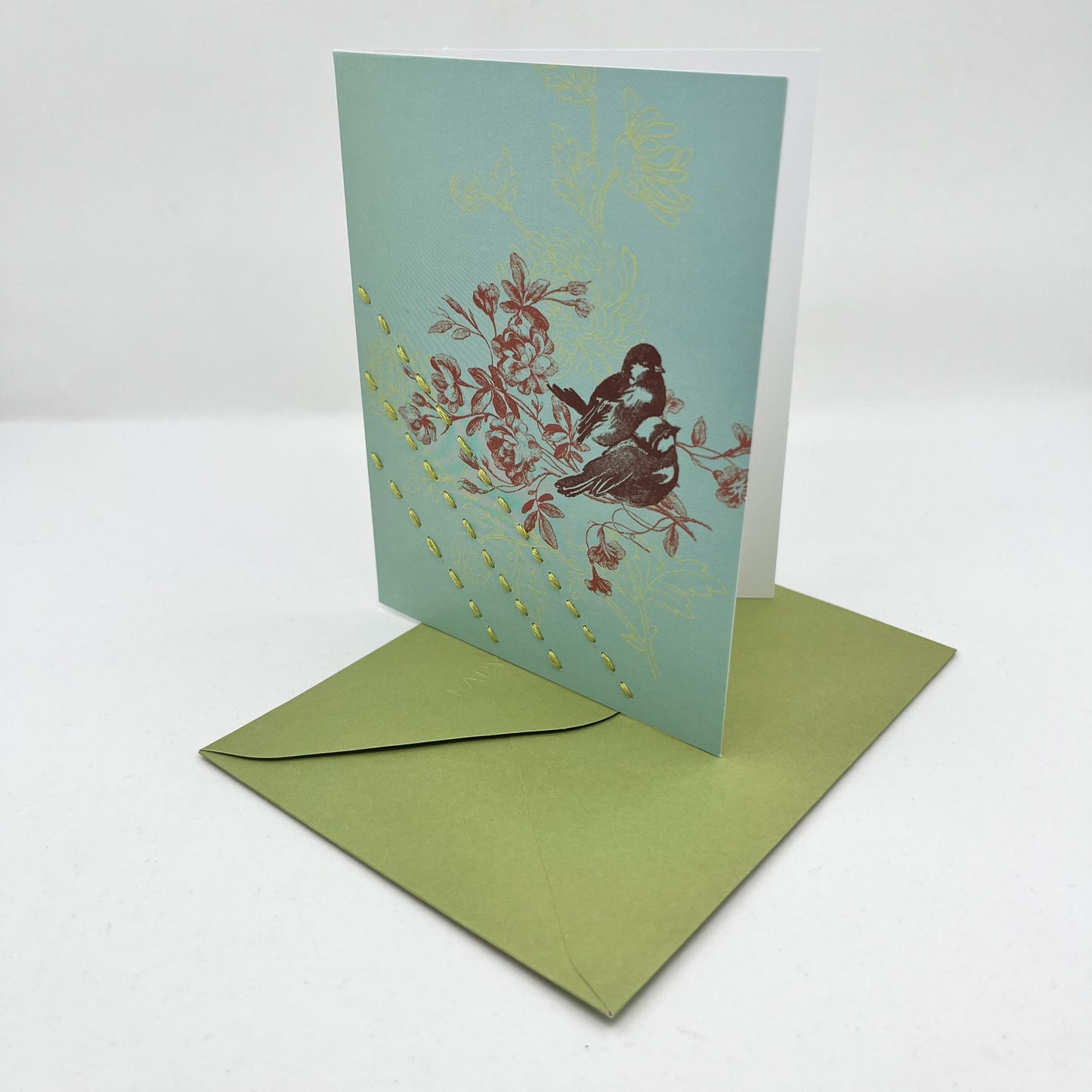 a robin's egg blue greeting card standing upright on a green envelope with a sparrow and flowers printed on it in reds and chartreuse, hand stitched over with 3 rows of running stitches in chartreuse, diagonally over the bottom left corner