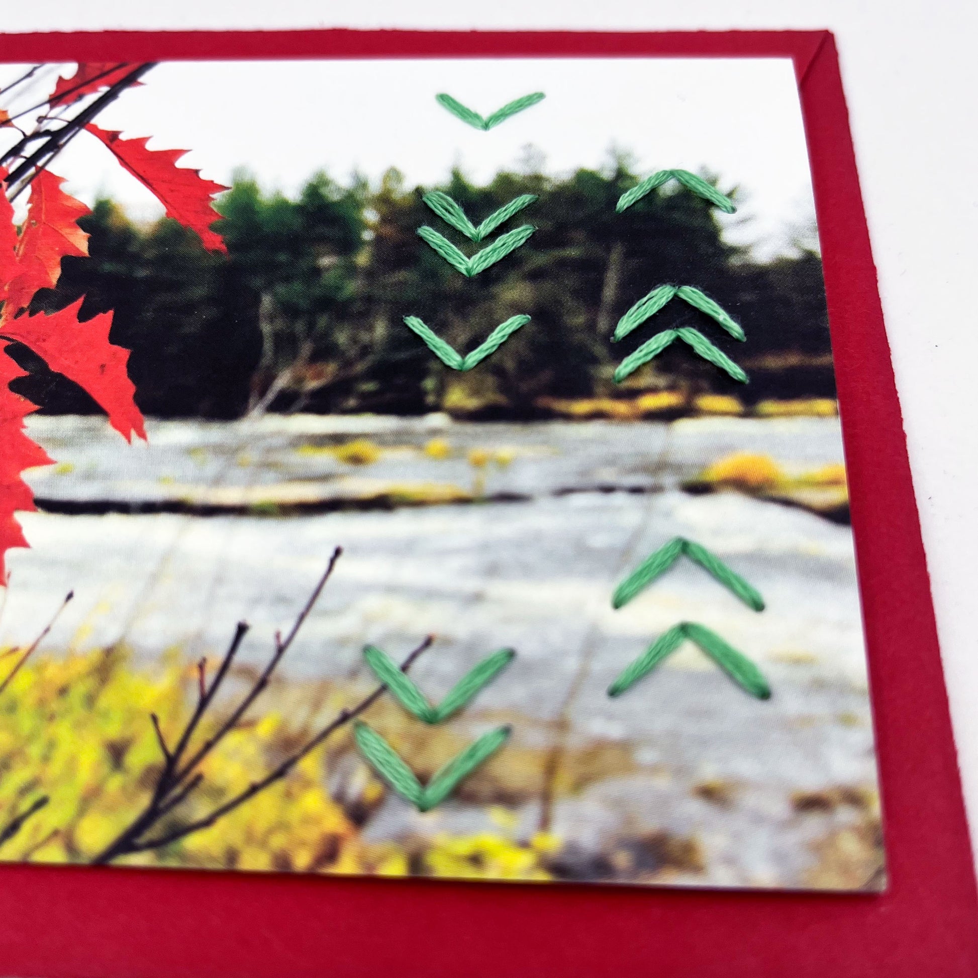 Greeting card flat on an envelope. Photo of red leaves. Rows of green chevron stitches along right side card