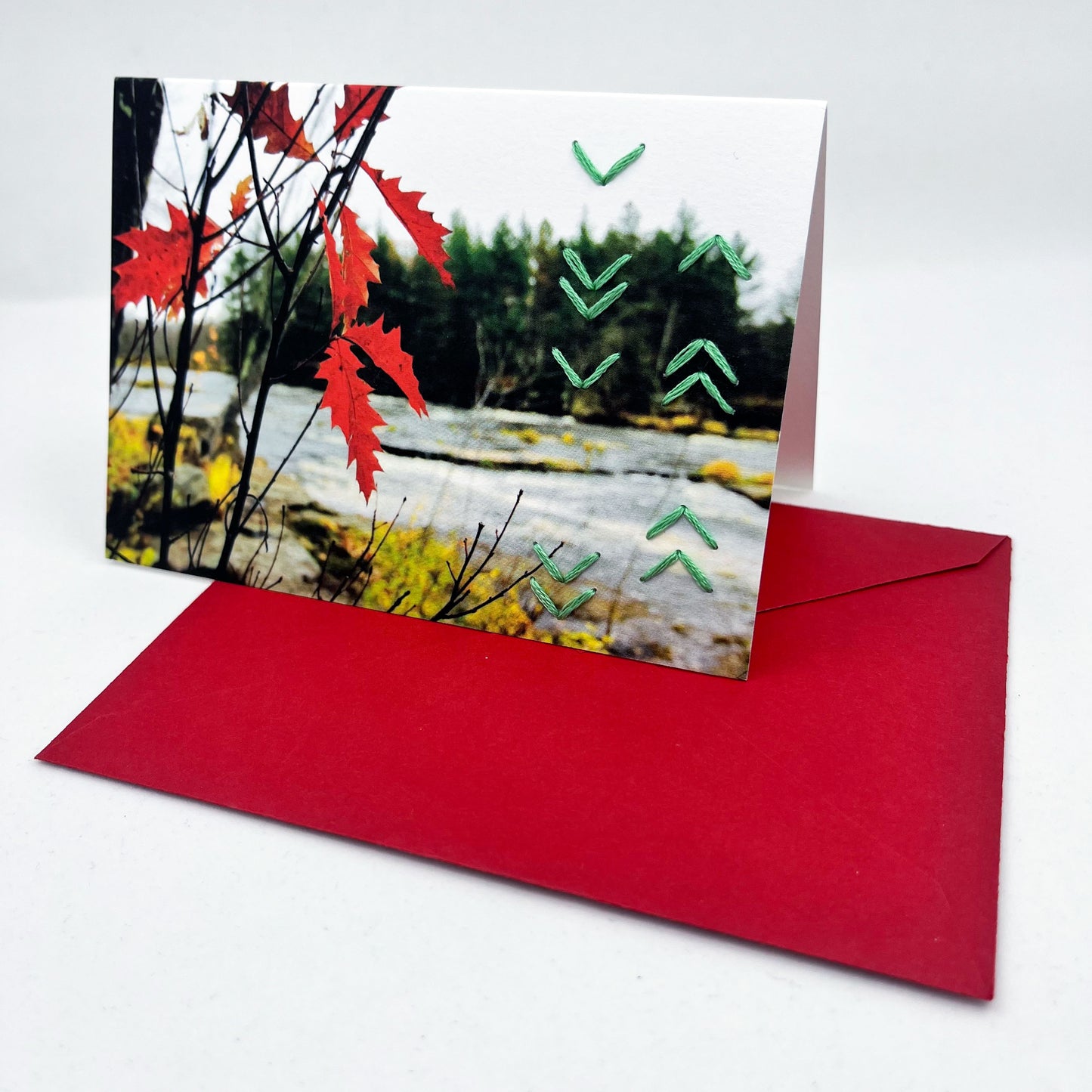 Greeting card standing upright on an envelope. Photo of red leaves. Rows of green chevron stitches along right side card